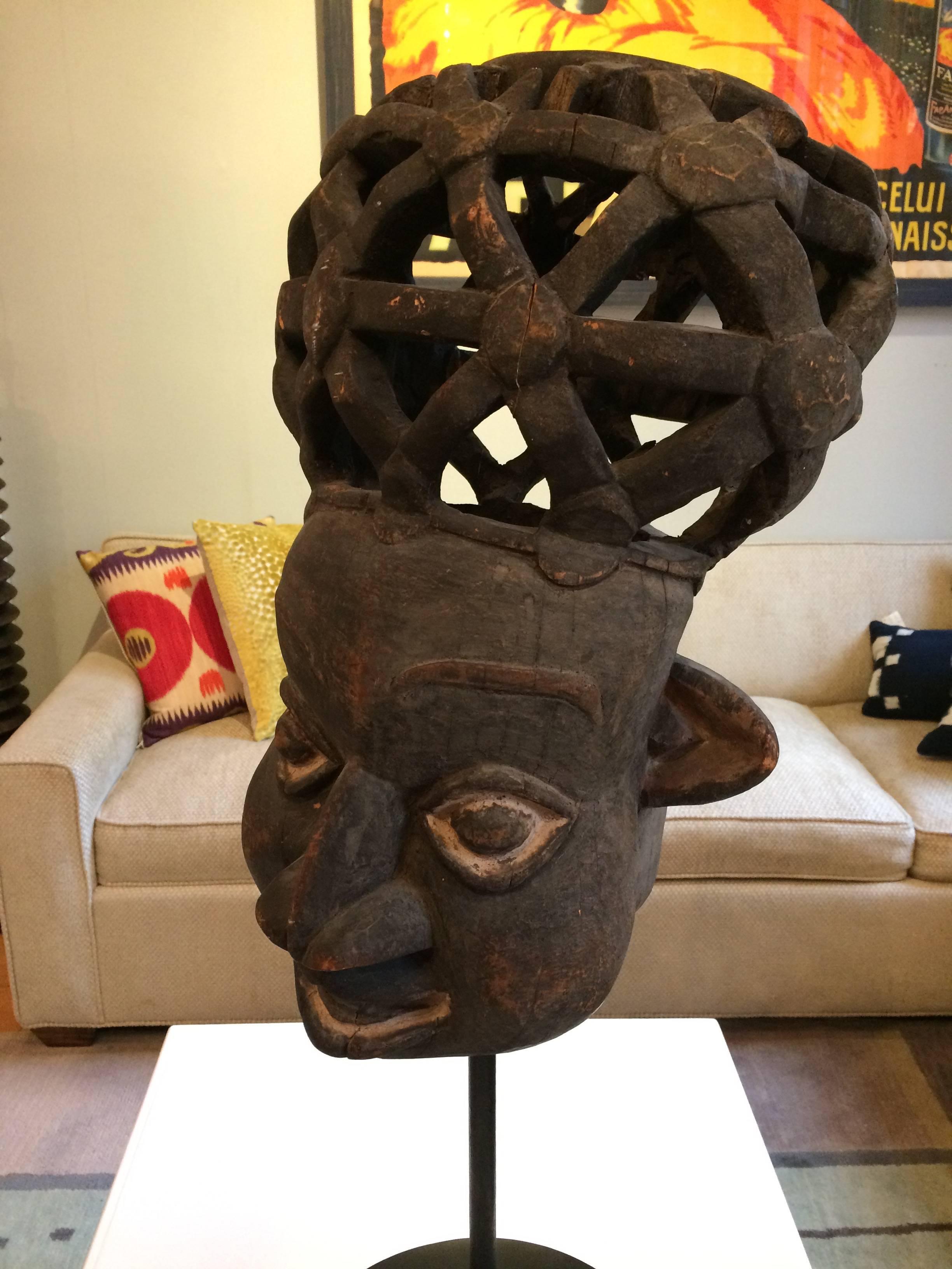 Étonnant masque africain sculpté à la main dans le bois, représentant une femme portant un panier en treillis sur la tête. Présenté sur un support personnalisé (inclus).