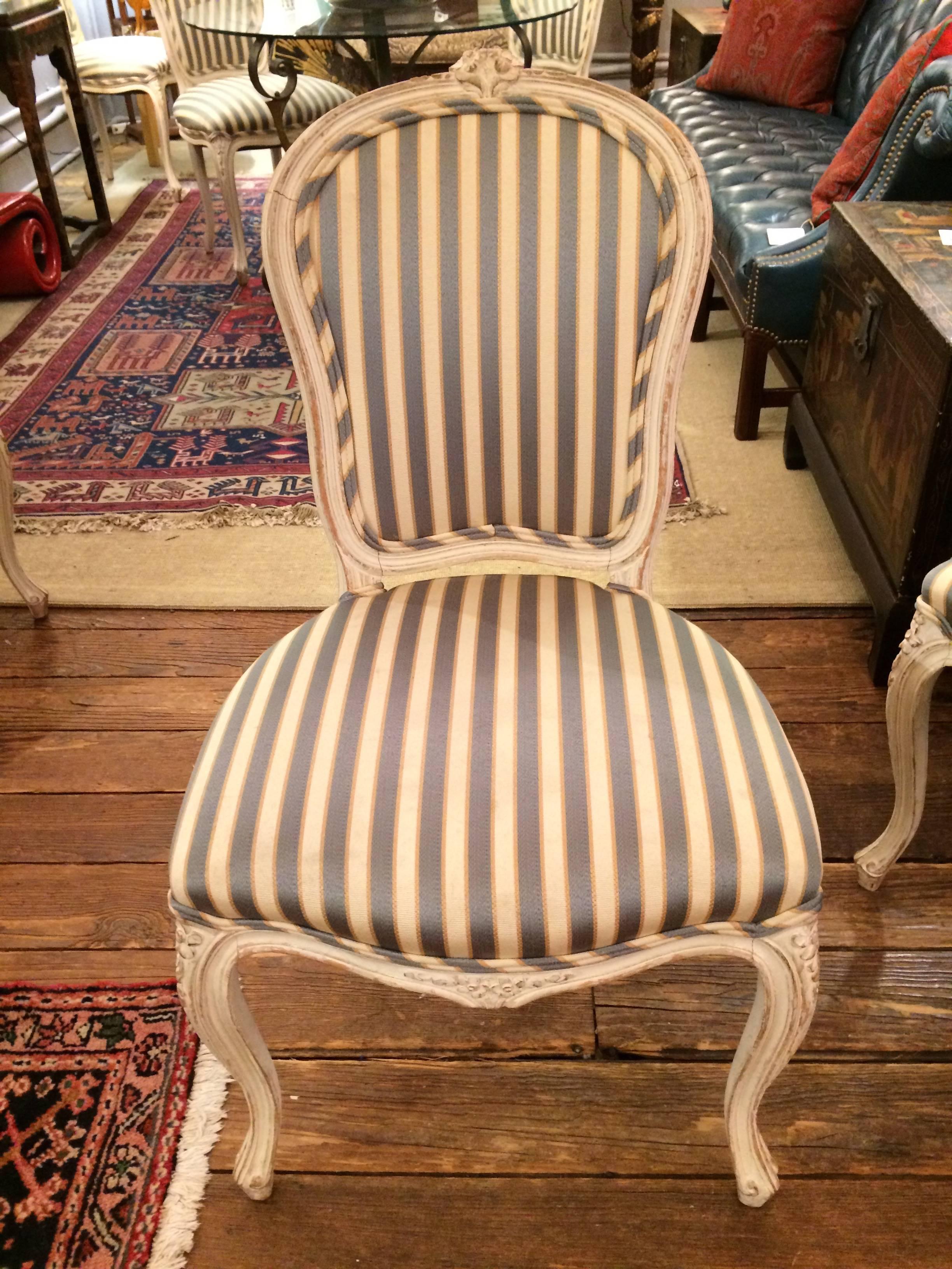 Elegant set of four hand-painted carved wood dining chairs having a slightly distressed finish, Classic French style, with two armchairs and two side chairs, upholstered in a blue and cream stripe. Upholstery has age appropriate wear.
Side chairs