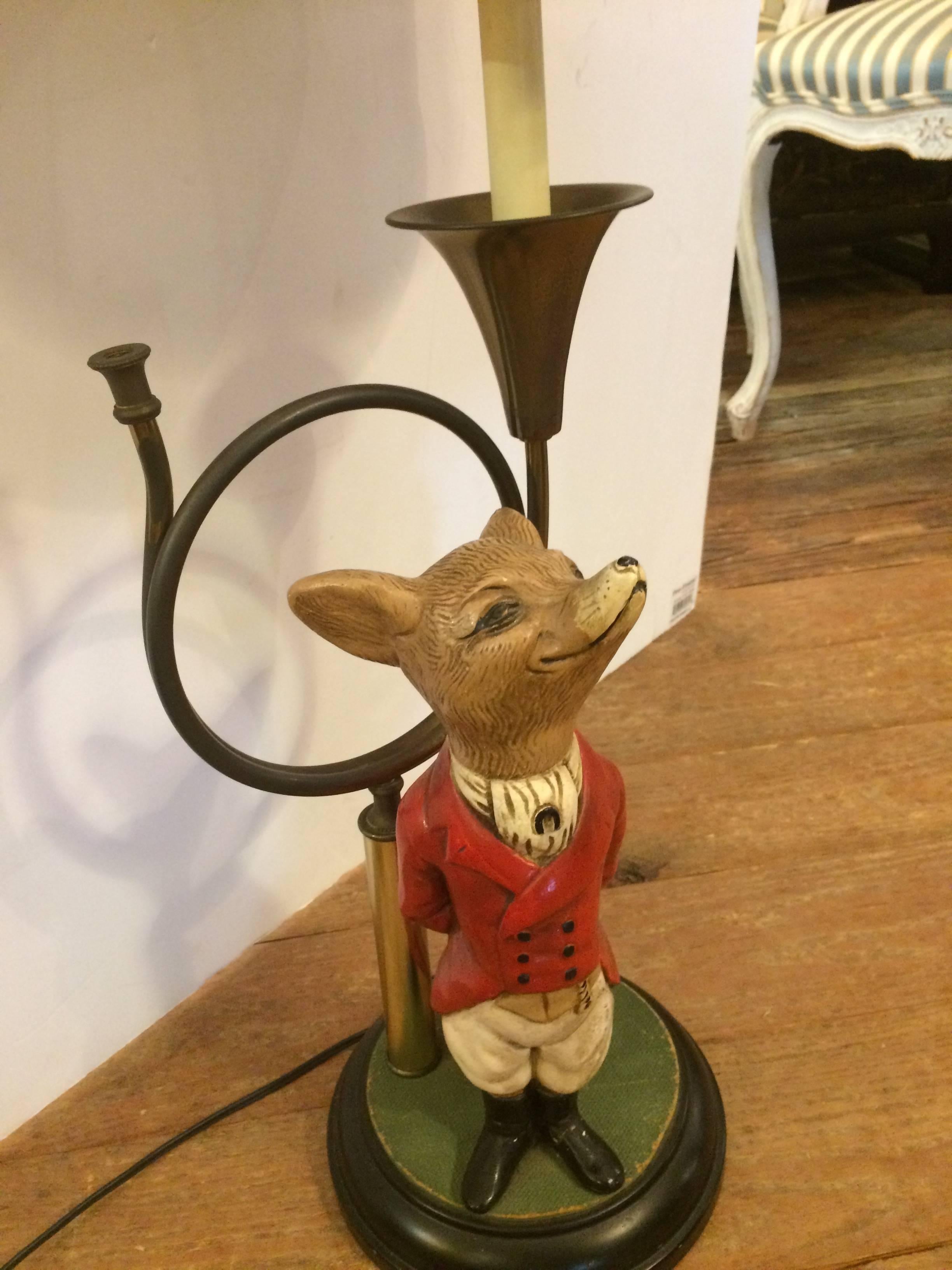 A show stealer adorable table lamp with libaryish feel having a carved painted composite fox figure dapperly outfitted in red coat and black boots, standing in front of a brass French horn. Base is 8