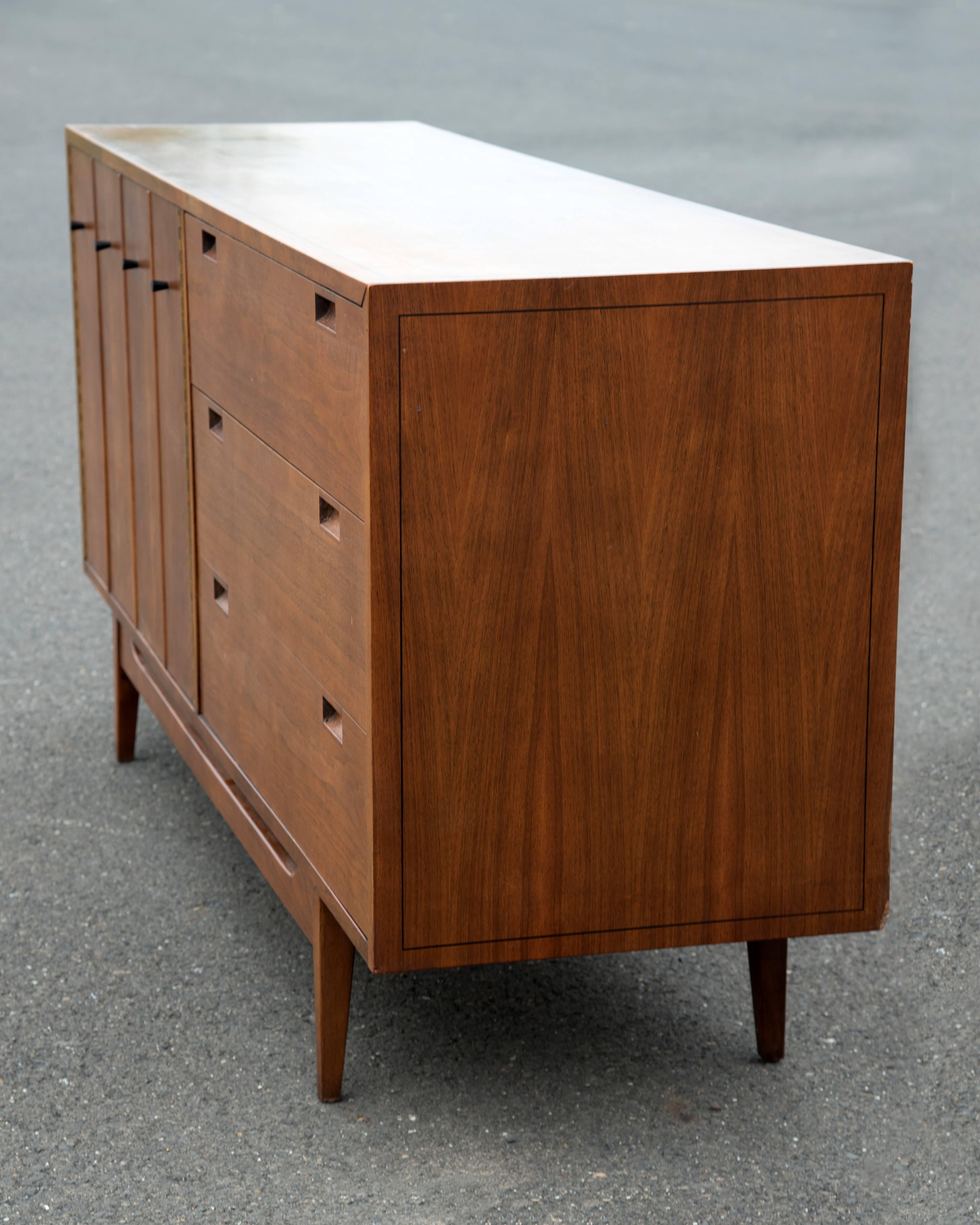 A sexy sleek American of Martinsville dresser having six ample drawers, cleverly designed with three of them hidden behind panel doors. Recessed Campaign style handles. Gorgeous mid century modern quality craftsmanship.