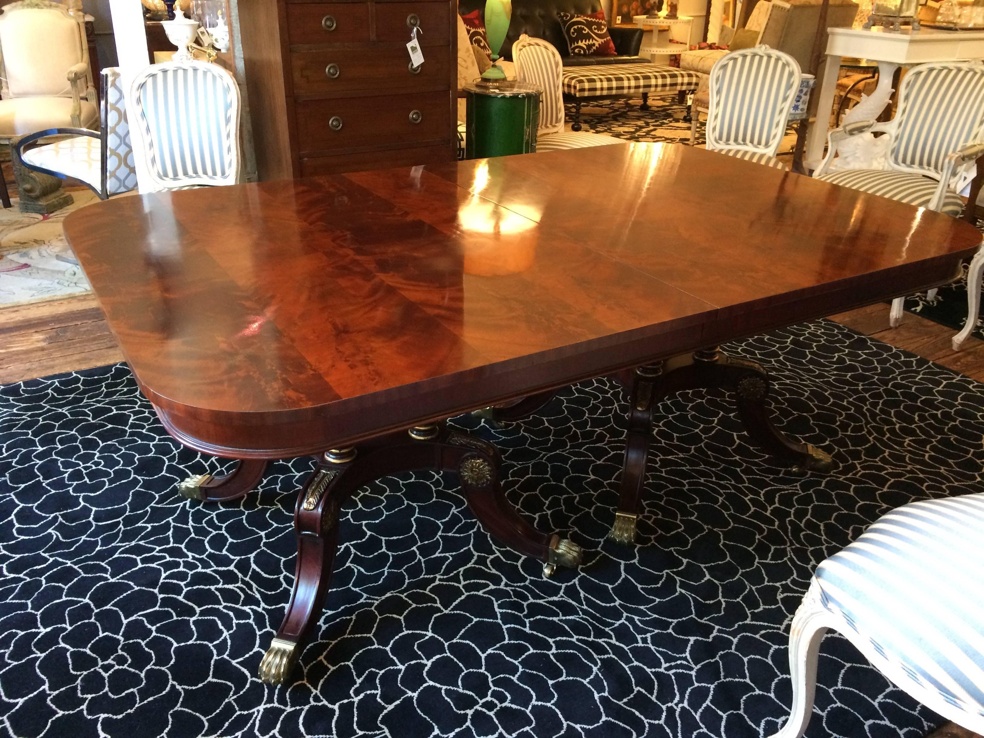 Gorgeous and stately dining table with richly grained mahogany top having two leaves and double Regency style four legged pedestals. The carved wood mahogany pedestals are beautifully adorned with gold paw feet, acanthus leaves and medallions. By