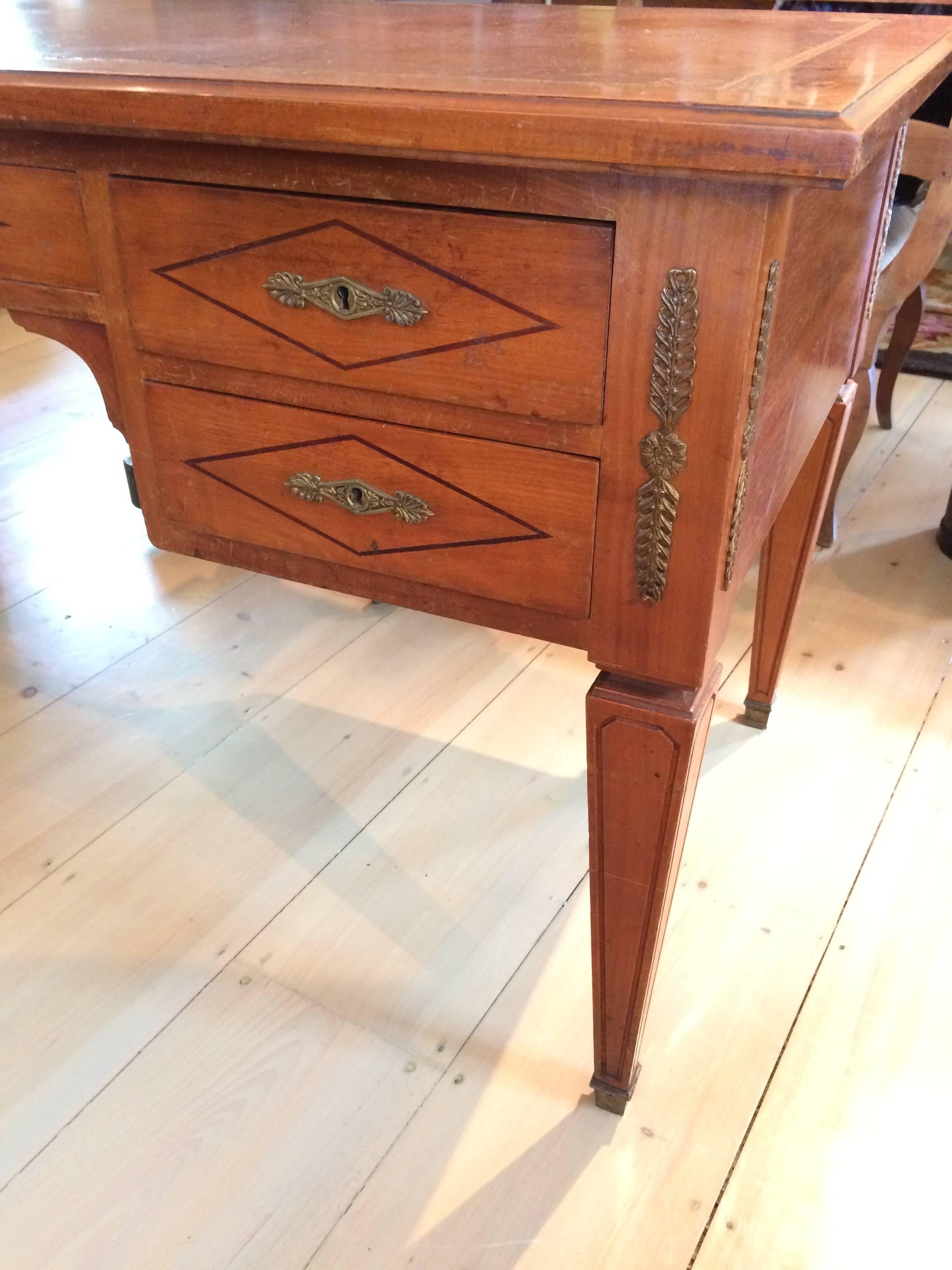 Antique walnut French Louis XVI style desk having its original embossed leather work area with a leafy gilt border. The desk extends by a hidden leaf on the right side of the desk and is opened by a decorative gold pull. The front of the desk has