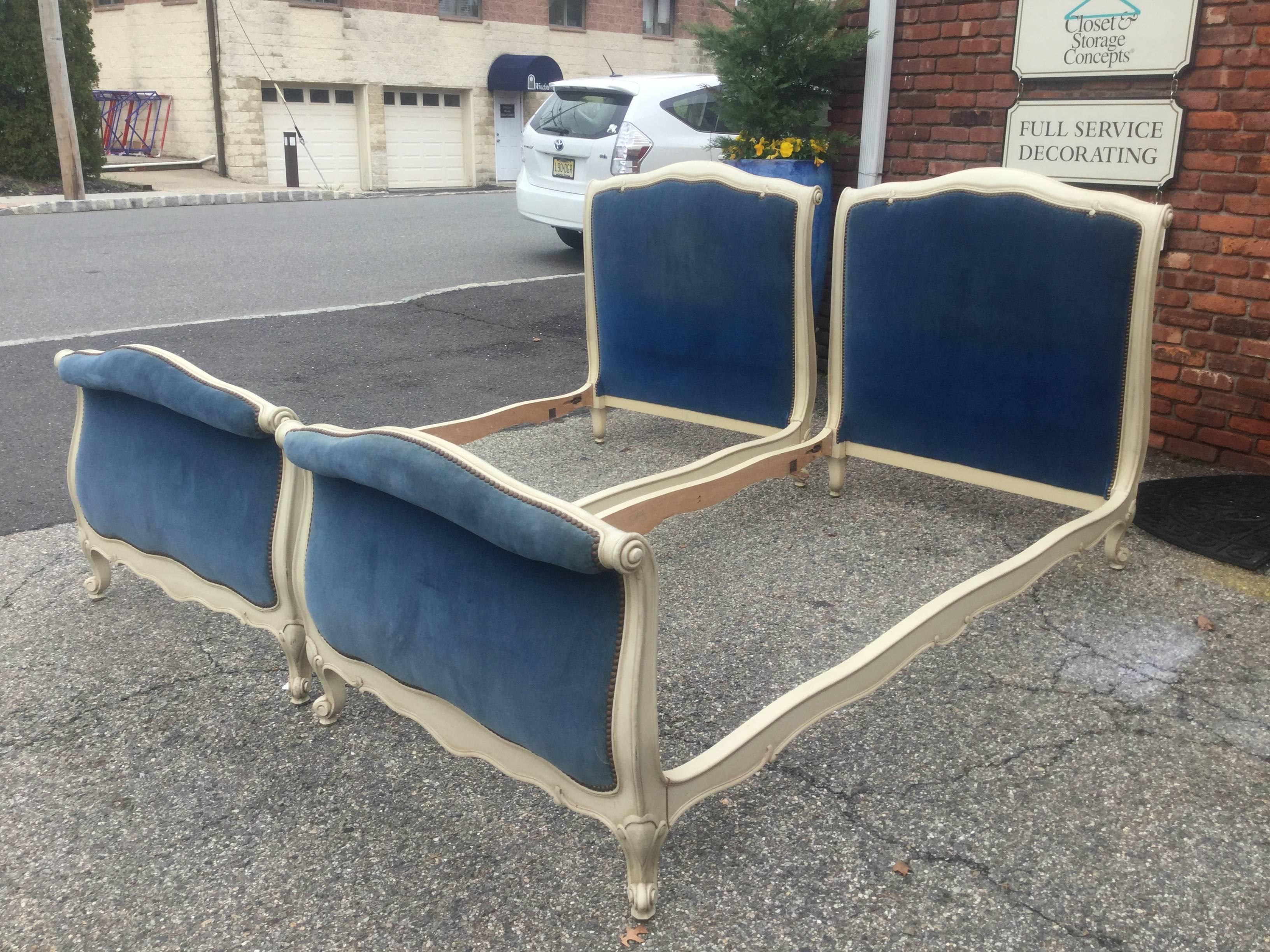 Pair of French Louis XV style painted beds retaining their original
off-white paint with scroll motif on the headboard and footboard with a cabriole foot. Upholstered in a vintage rich blue velvet fabric with brass nail-heads. Upholstery is in very