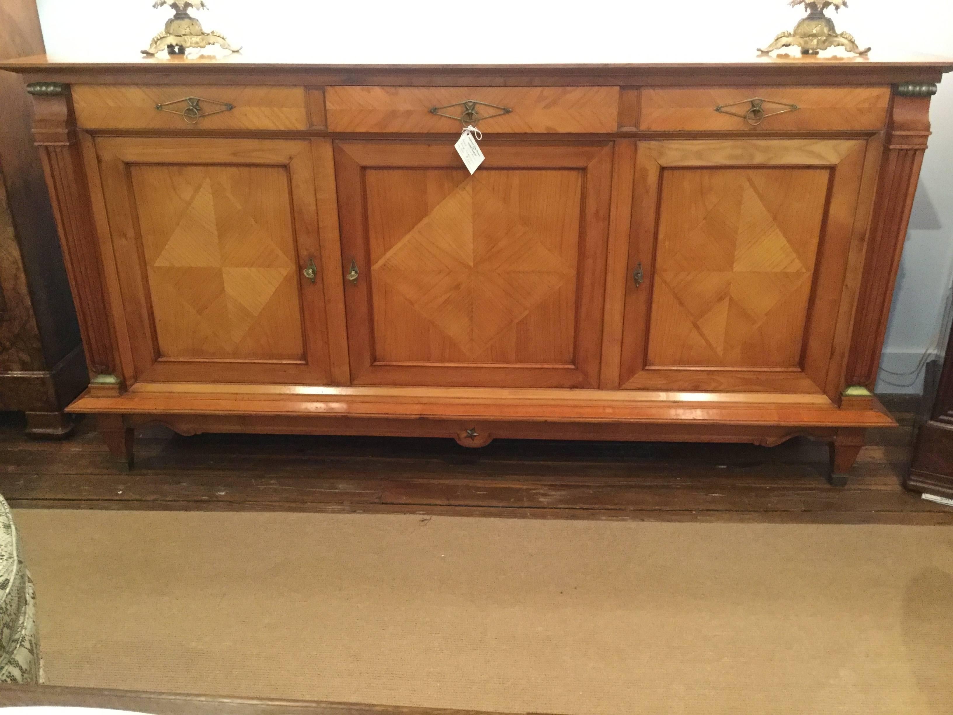 Handsome French cherry credenza in the Directoire style. Made of solid French cherry, this piece features three doors and three drawers for storage. The door panels are decorated in a diamond-shape pattern. Original brass hardware enhance the