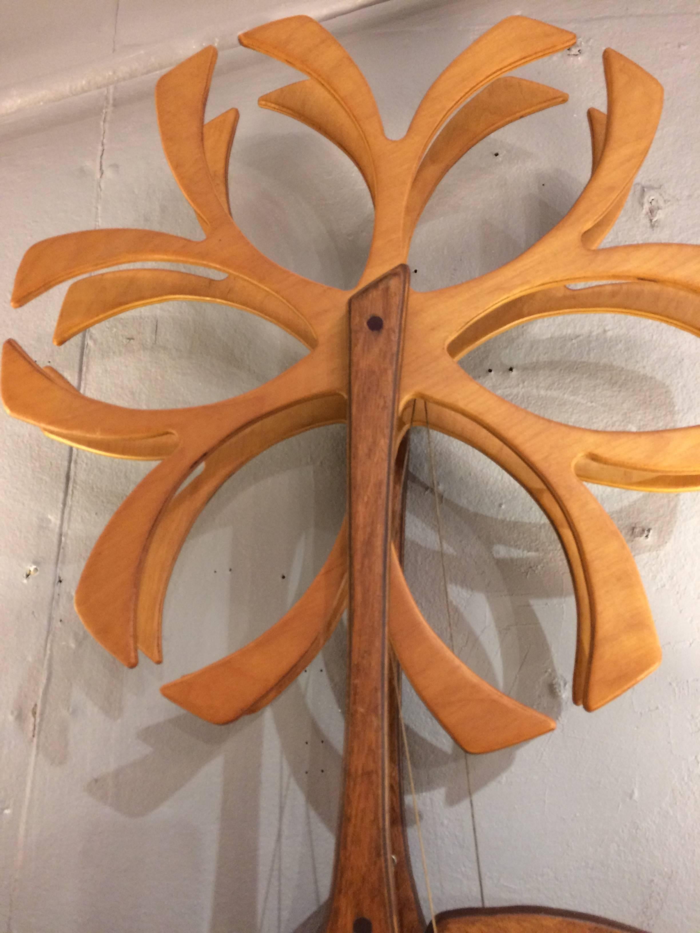Eye-catching organic sculpture made from wood with central circular snowflake like mandala, connecting by string to other pieces that rotate, reminiscent of the inner workings of a clock. Two pulley like pieces are suspended by string 59 inches from
