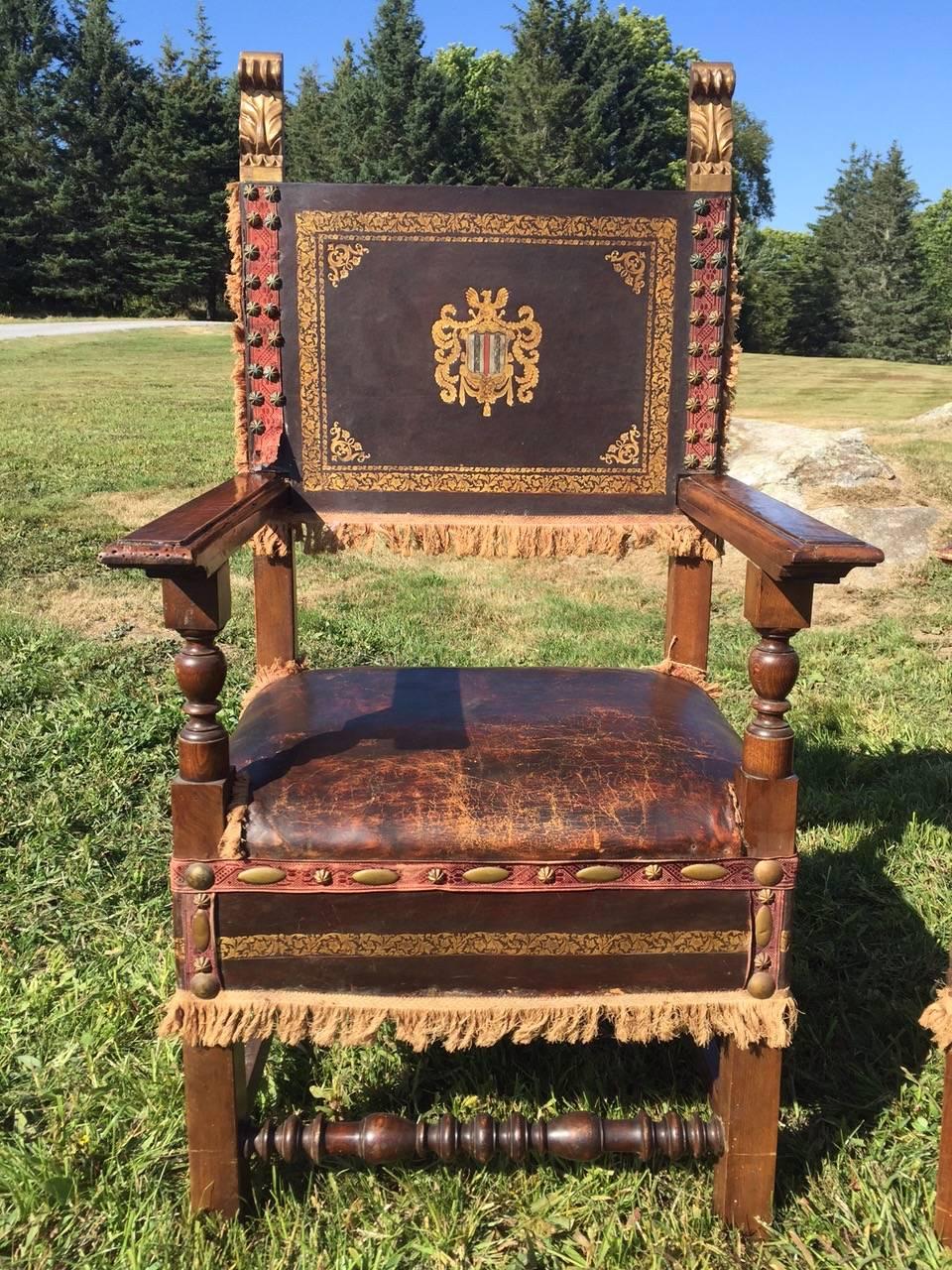 Very impressive grand and fancy pair of midieval large throne chairs having elaborately tooled leather carved walnut frames, brass nailheads and decorative fringe.
They have two beautiful gold acanthus leaf finials on each chair. The dimensions of