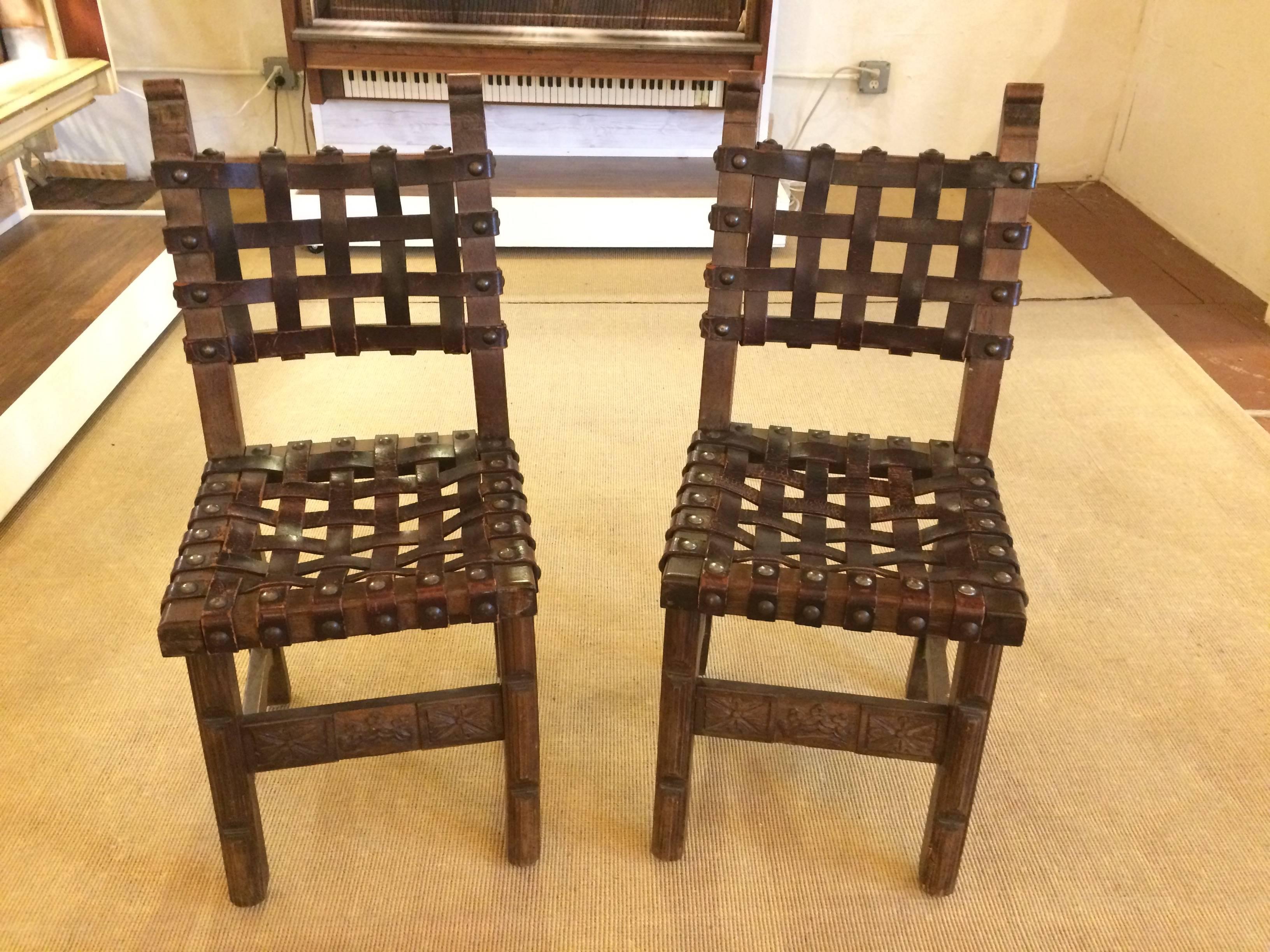 Two antique Spanish side chairs having wonderfully carved wood bases and rich heavy woven strap leather seats and backs with big masculine nailhead studs. By Navarro Argudo, Spain. Leather has natural aged distressed patina.
