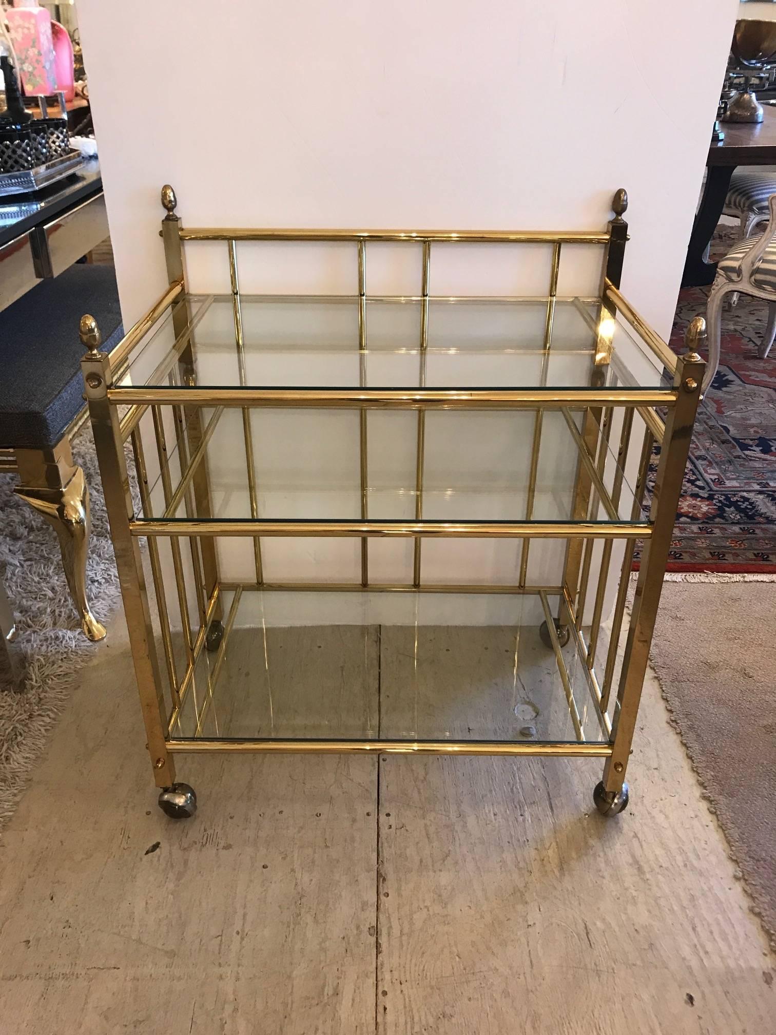 Stylish brass bar cart or server having three glass tiers and handsome acorn finials, on casters.
 
