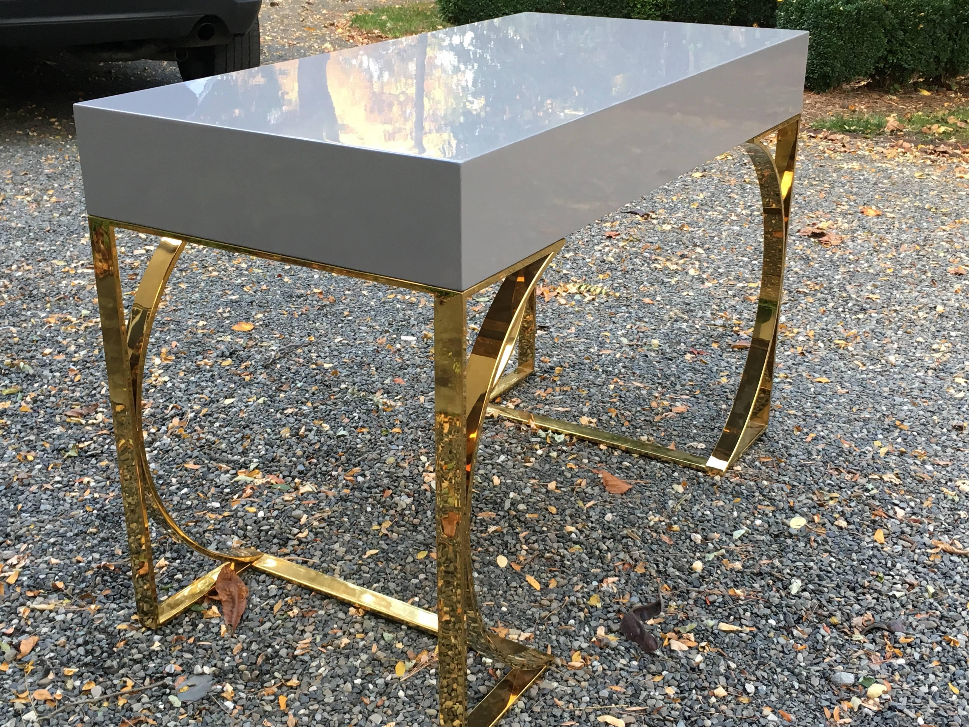 Sophisticated and sexy lacquered desk in battleship grey, having double curved legs in heavy solid brass. The two drawers are also lacquered grey inside and out.