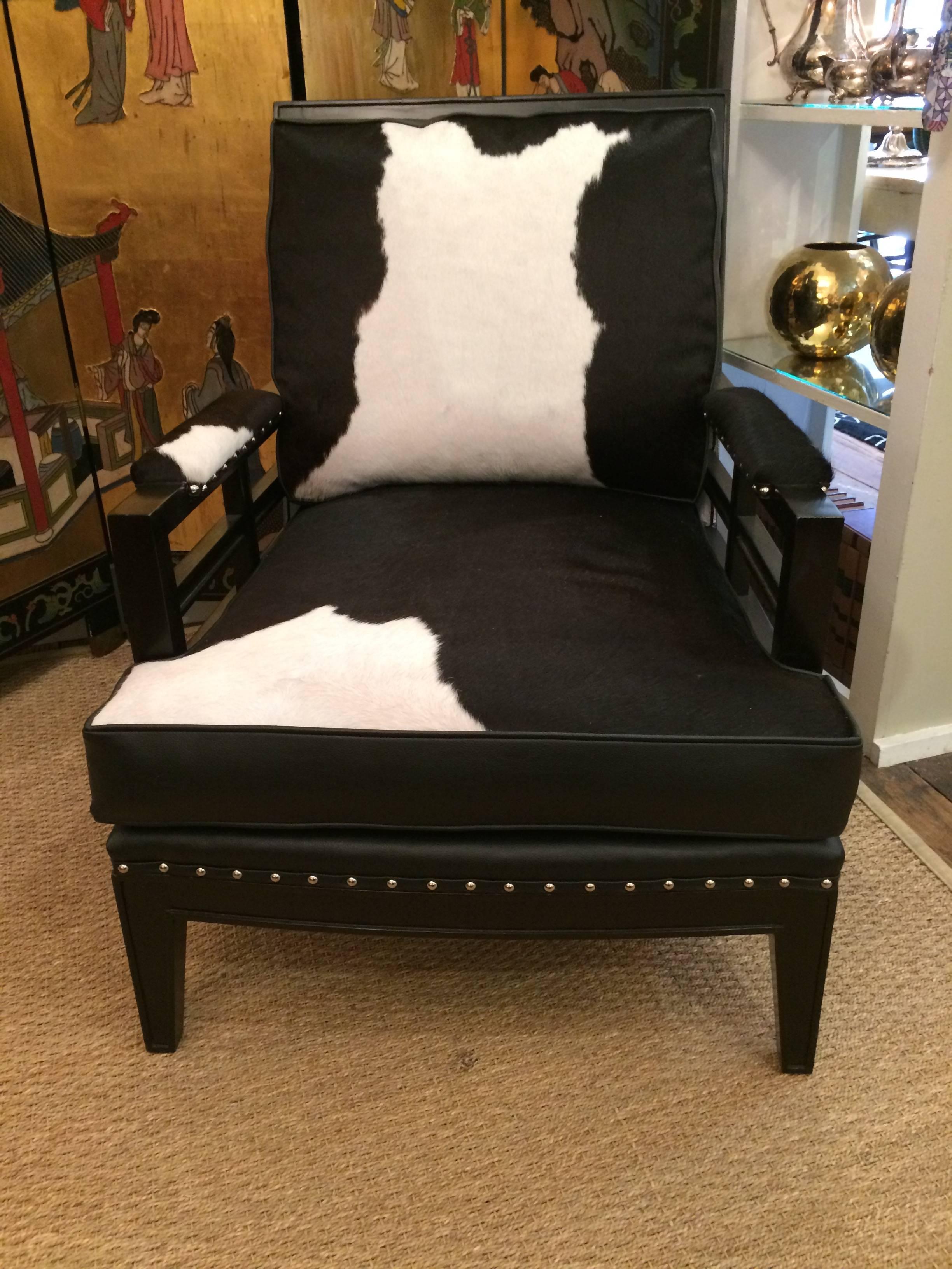 Fabulously chic custom club chair and ottoman having ebonized wood and a mix of black leather and black and white cowhide upholstery, finished with nailheads. The ottoman has a stretcher style base and measures 26 W x 19 D x 17 H.