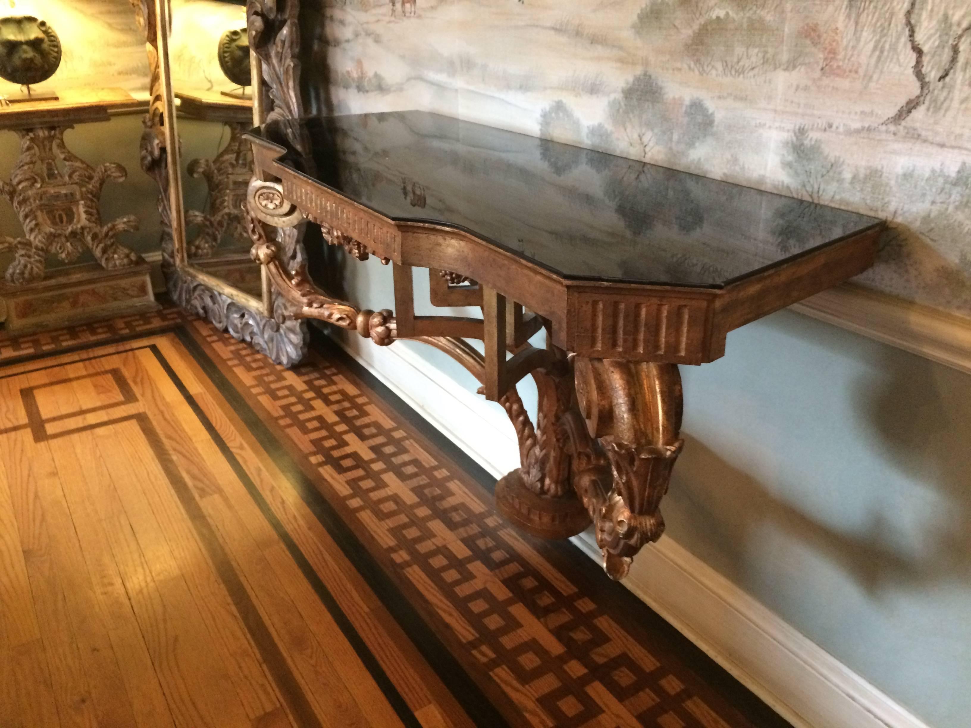 Elegant carved giltwood console with wonderful curlicue supports and contemporized with a piece of black glass on top. Must be secured to wall.