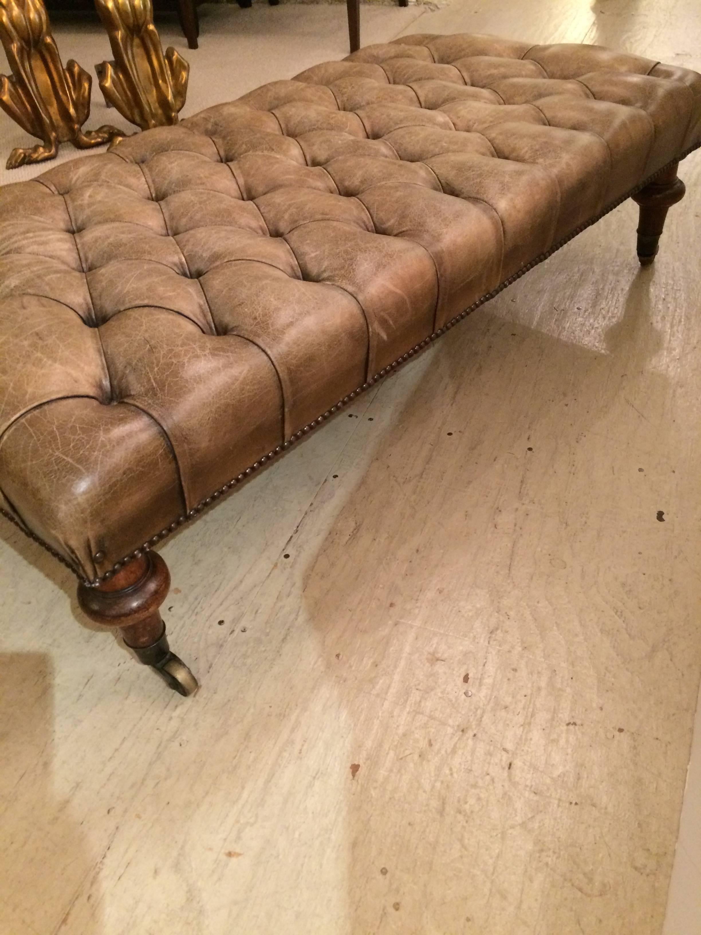 Buttery distressed tufted leather ottoman, bench or coffee table in a wonderful brownish taupe luggage color, with muted brass studs, handsome turned fruitwood legs and brass casters. Top of the line rich and elegant antique from London.