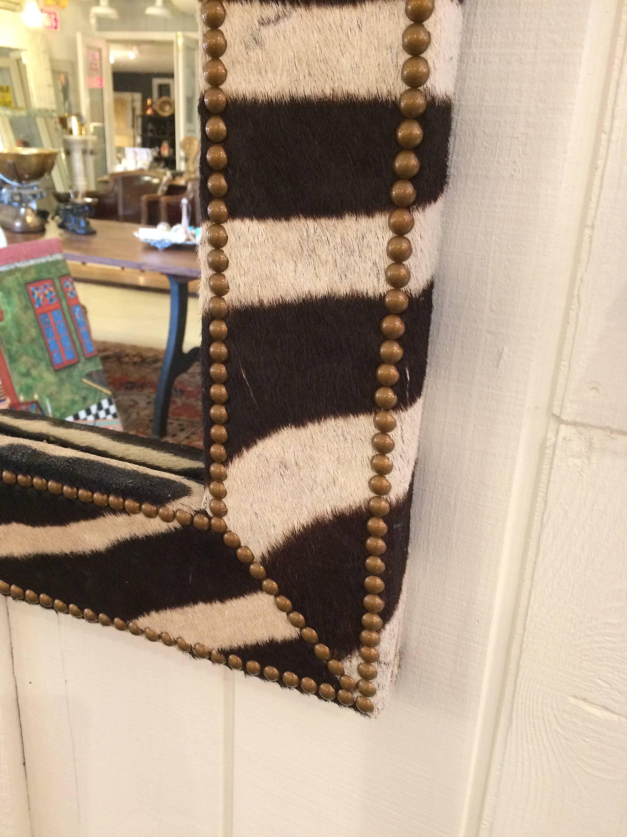 Custom-made fabulously dramatic mirror with a chunky zebra hide upholstered frame finished with brass nailheads.