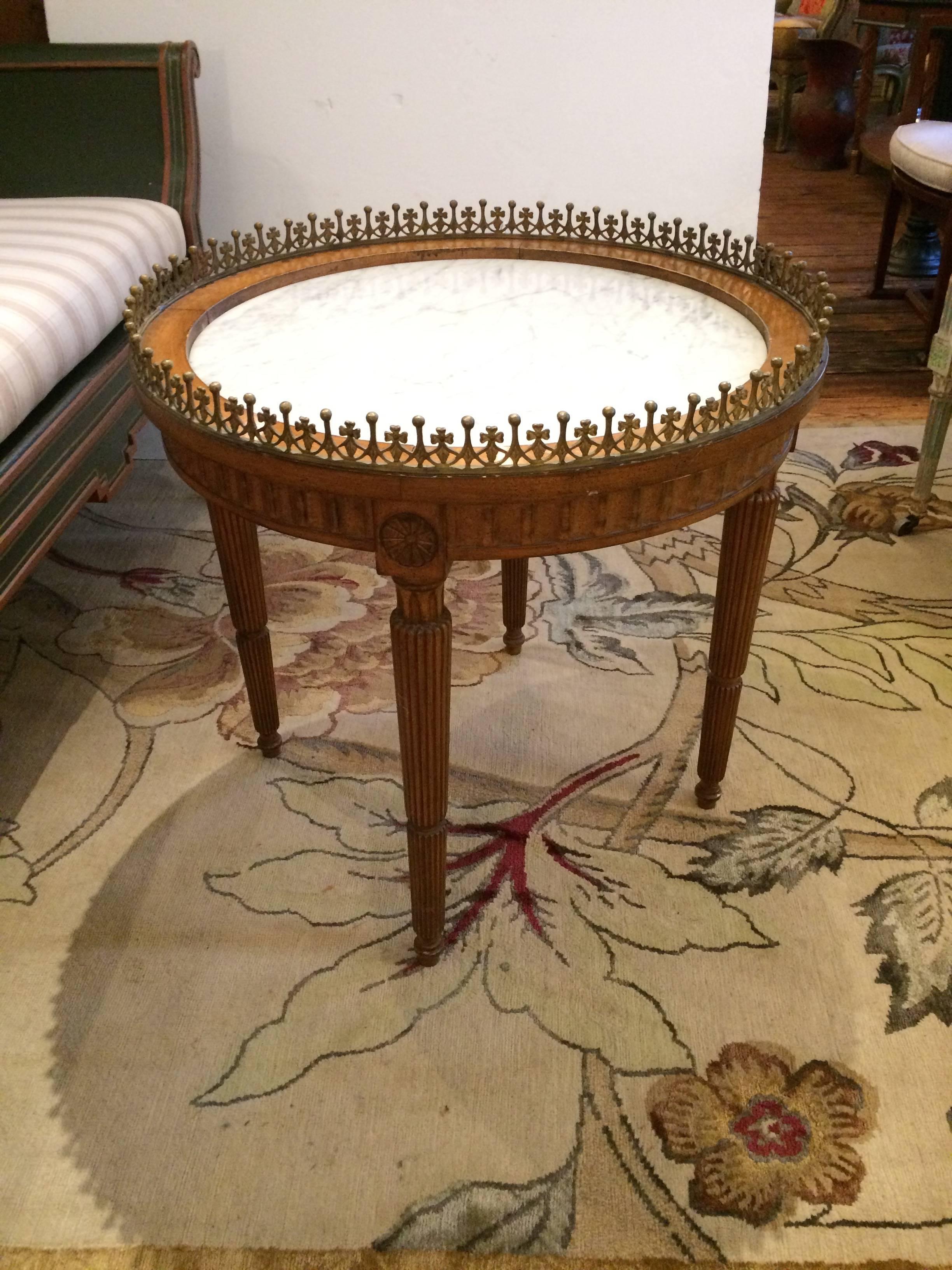 Gorgeous round carved walnut cocktail or side table having inset white marble top, tapered reeded legs, and special very decorative bronze gallery around the periphery.