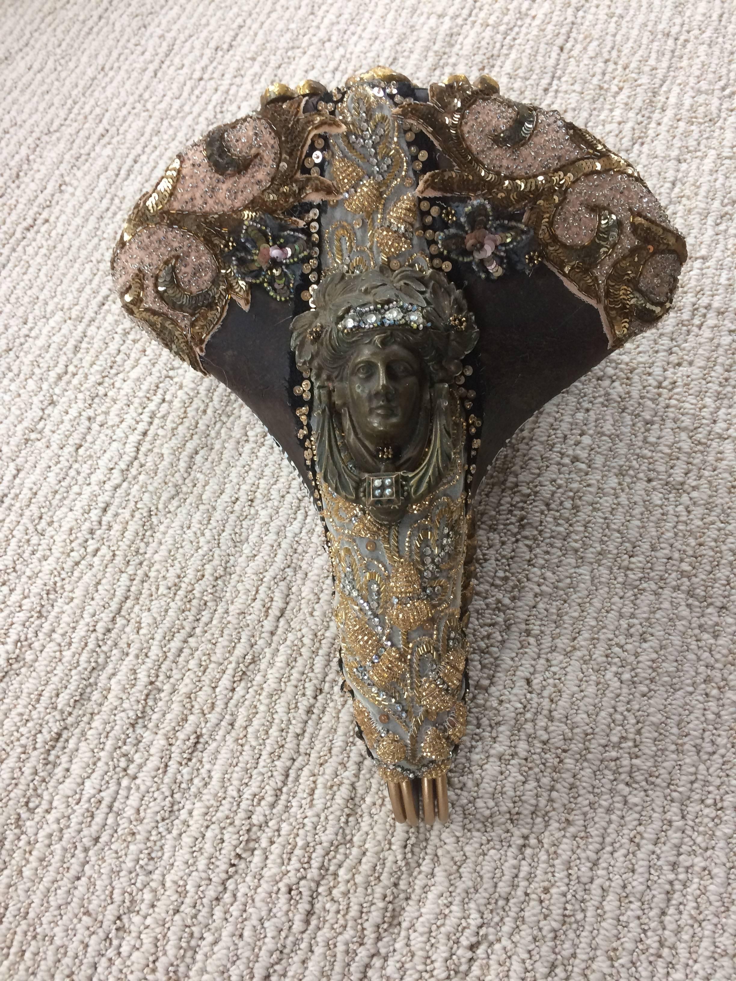 Fabulously imaginative found object sculpture on a vintage bicycle seat mined in a small antiques store in Amsterdam, having bronze door knocker, beaded bits and pieces from couture evening gowns, giltwood fragments and hand-painted