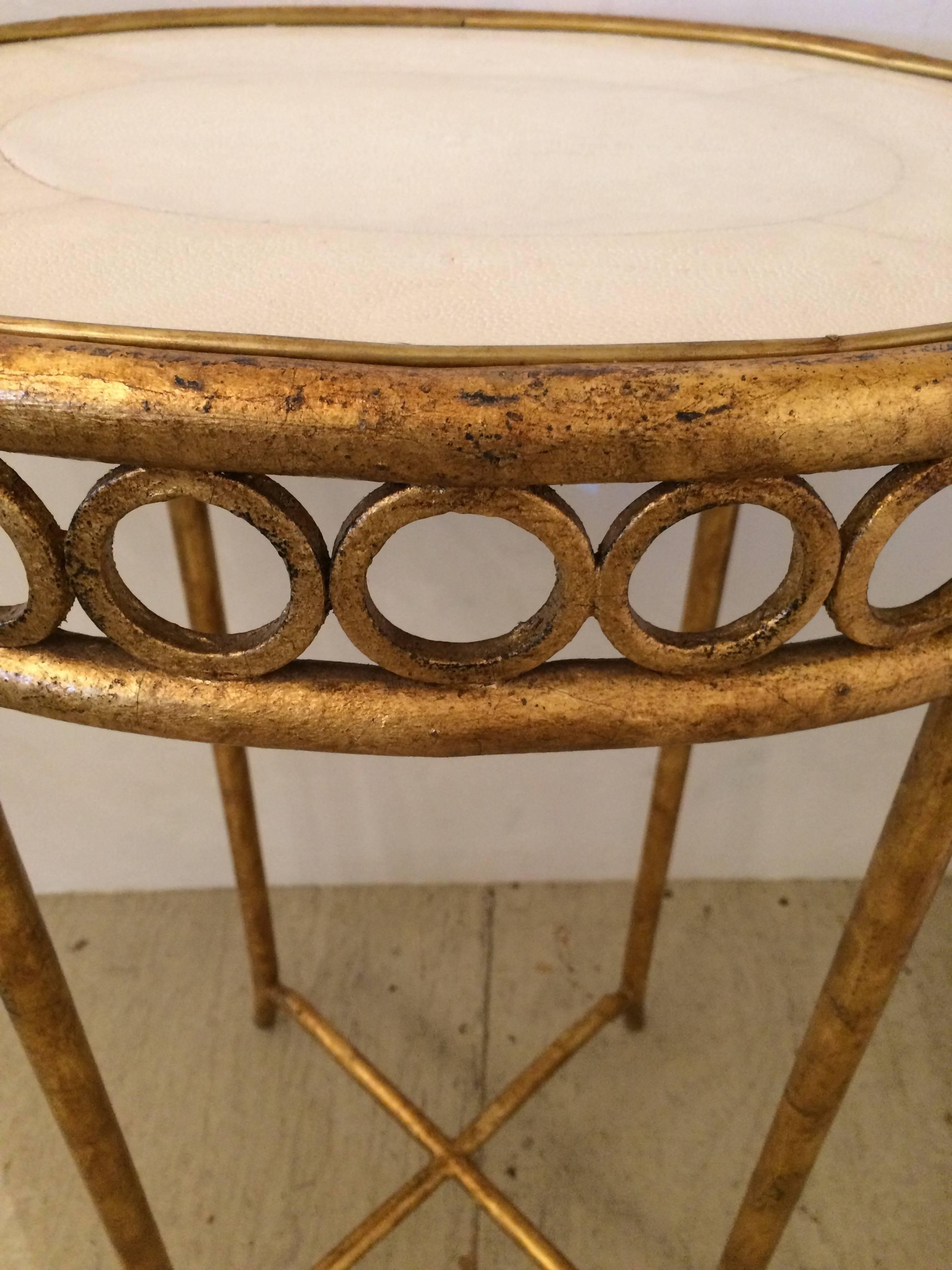 Glamorous oval side or end table having a gilt iron base with circle motif and faux shagreen cream colored top.