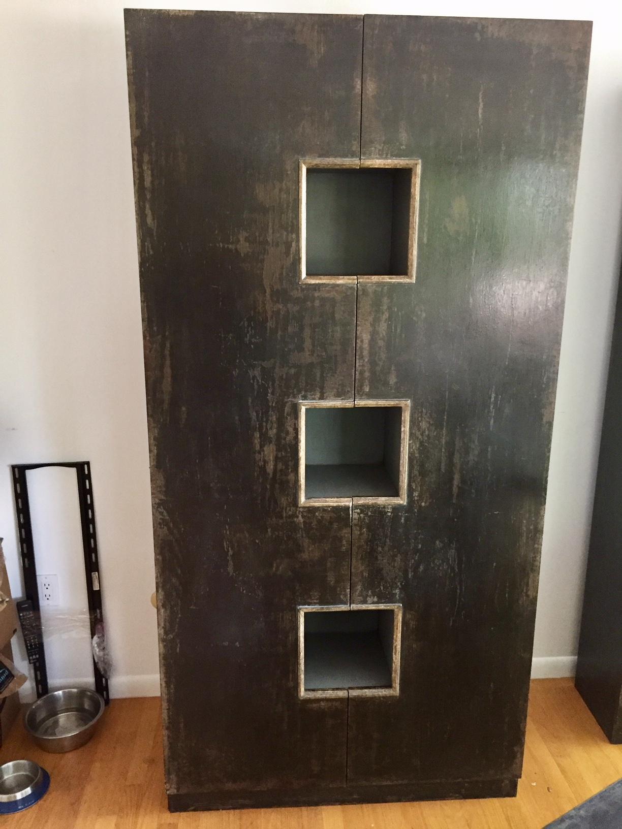 A handsome cabinet with distressed dark brownish grey finish and beautiful inset square blocks outlined in bronze to display objets d' arte. Two doors open to reveal grey painted interior with a fascinating complex of shelves.

