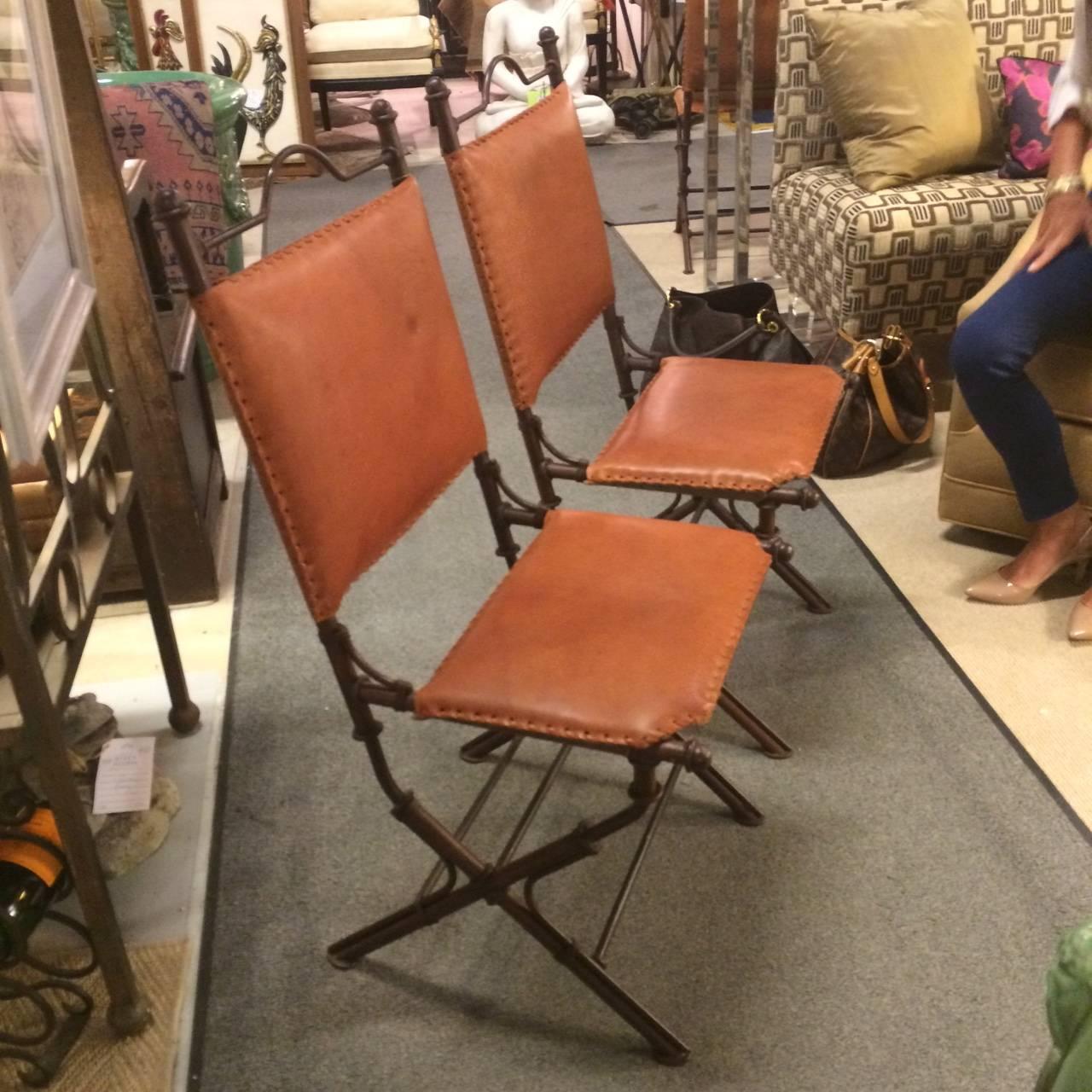 Four handsome Ilana Goor style campaign chairs having hand stitched saddle leather and brown wrought iron. Age appropriate marks to leather.