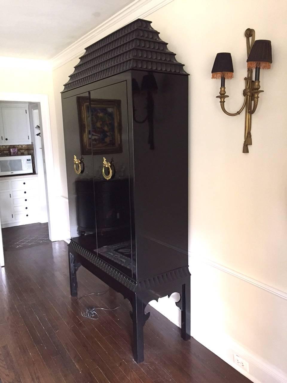 Sensational high gloss black laquer custom cabinet having pagoda style top, Chinese inspired design, gorgeous brass dragon motiffe pulls, mirrored interior back. Cleverly outfitted as a bar cabinet with wine rack, area to hang crystal glasses, a