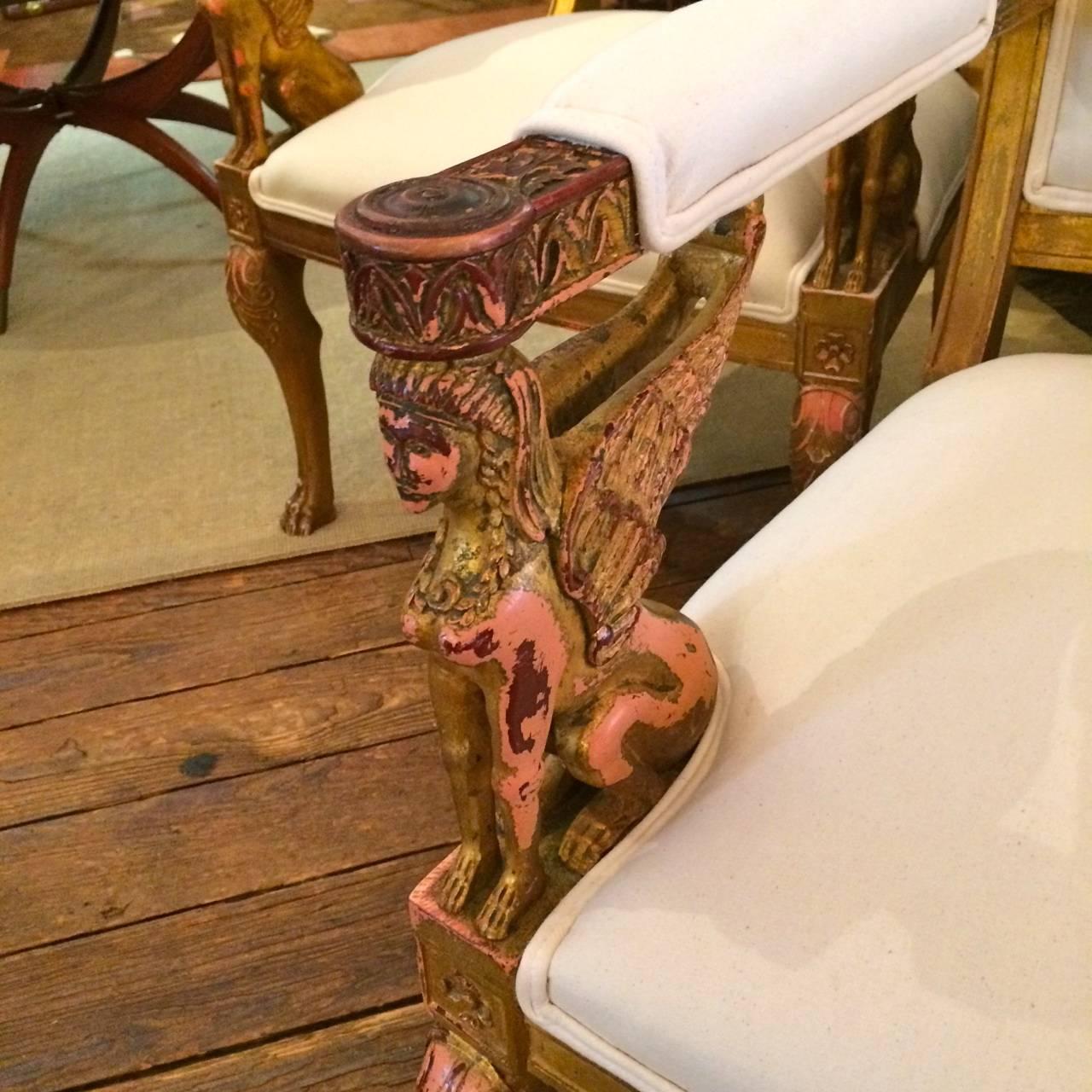Very unusual carved wood armchairs with original chippy paint in gold and salmon, gorgeous female winged figures support the arms, lovely curved legs and beautiful decoration at the top of the chairs. Just reupholstered in crisp creamy duck