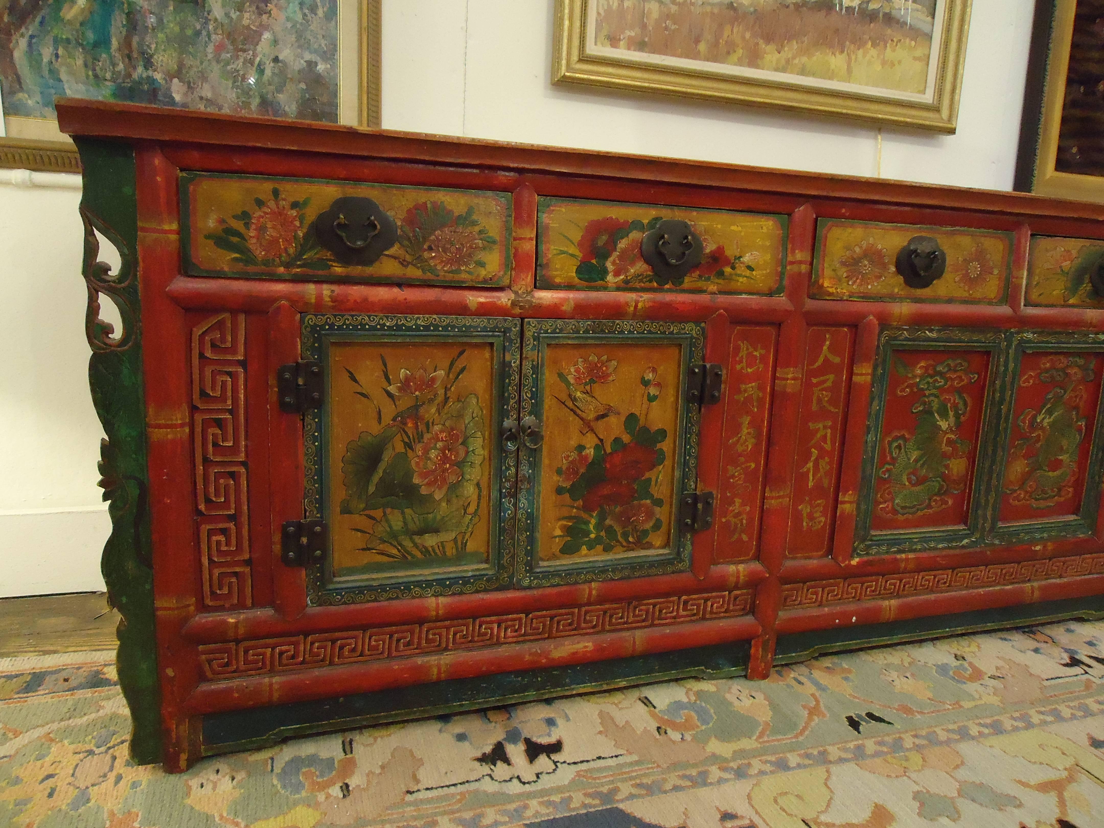 Very long hand-painted wooden cabinet with fabulous decoration in opposing colors of red and green with dragons, flowers, Greek key, etc. Original hardware and lots of storage including six drawers and two pairs of panelled doors that open to lots