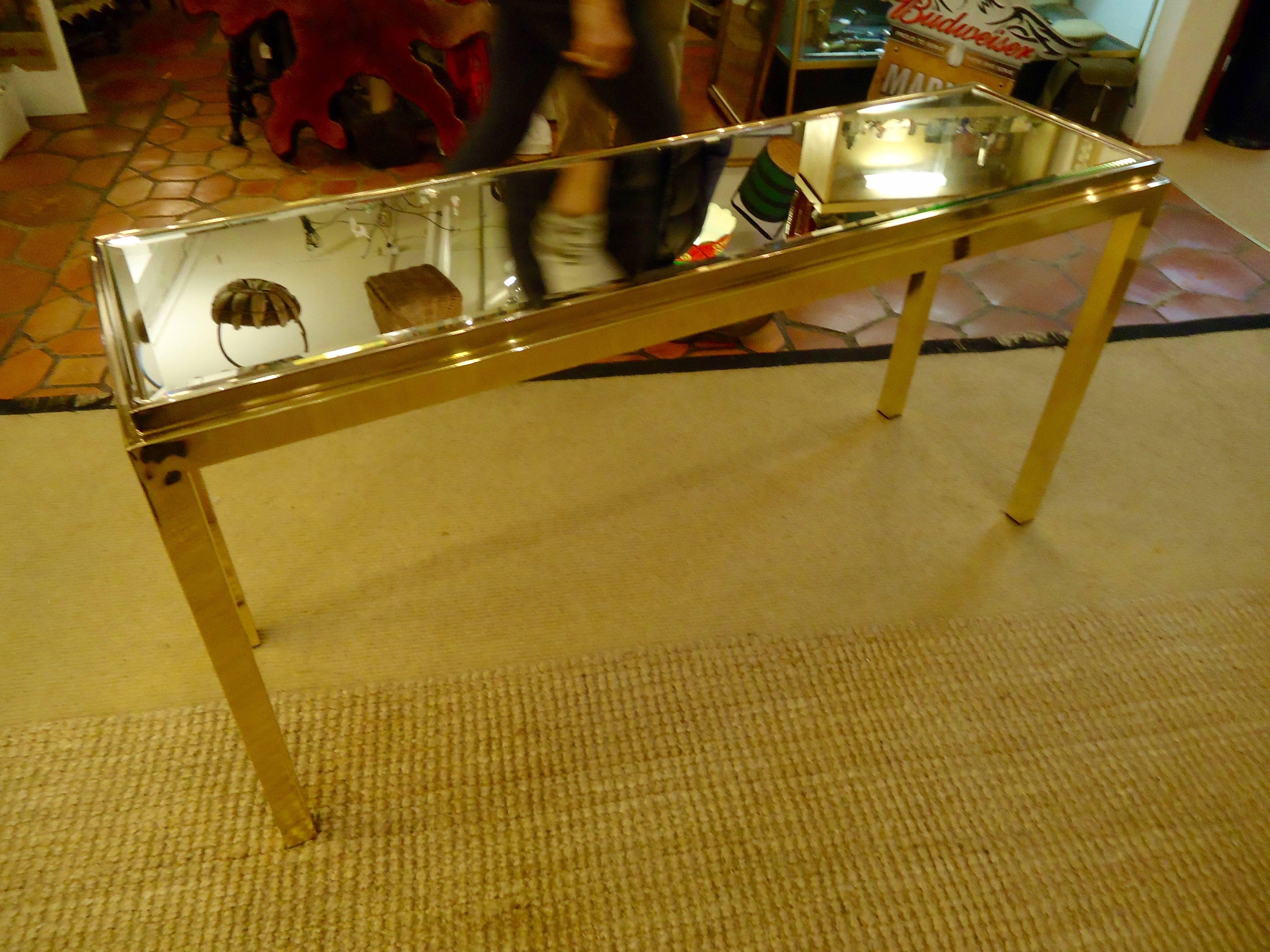 Sleek Mid-Century Modern console, diminutive and low in scale, superb behind a sofa. Good condition shiny bold brass and bevelled mirrored top.