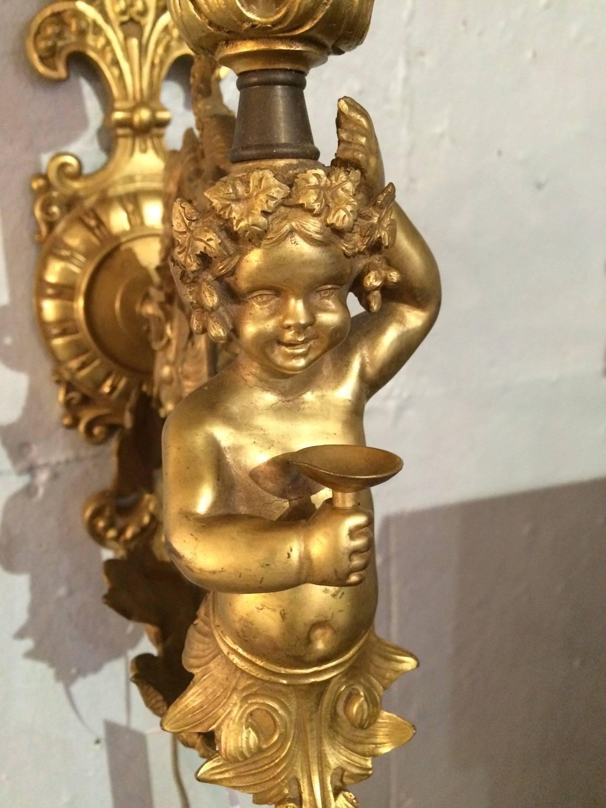 Ornate French bronze sconce having fleur de lis on top and bottom, dragon embellishment and charming cherub that balances the single shaded light on its head.