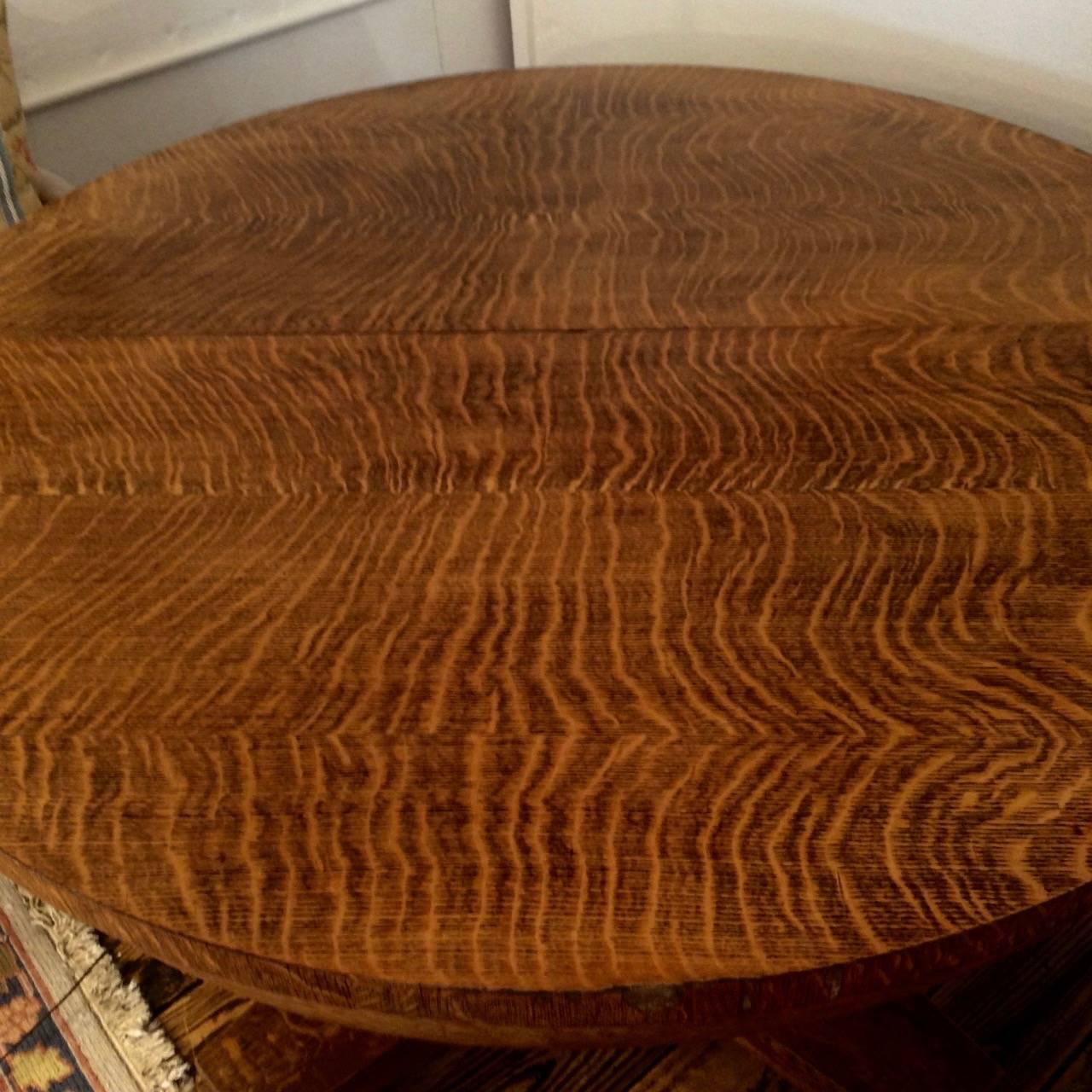 A charming, early 20th century, round dining table in the Arts and Crafts style with a gorgeous grained wood, center pedestal. It opens to receive two leaves, each 12.25 wide, so fully extended becomes a 69.75 oval. Leaves are not refinished to
