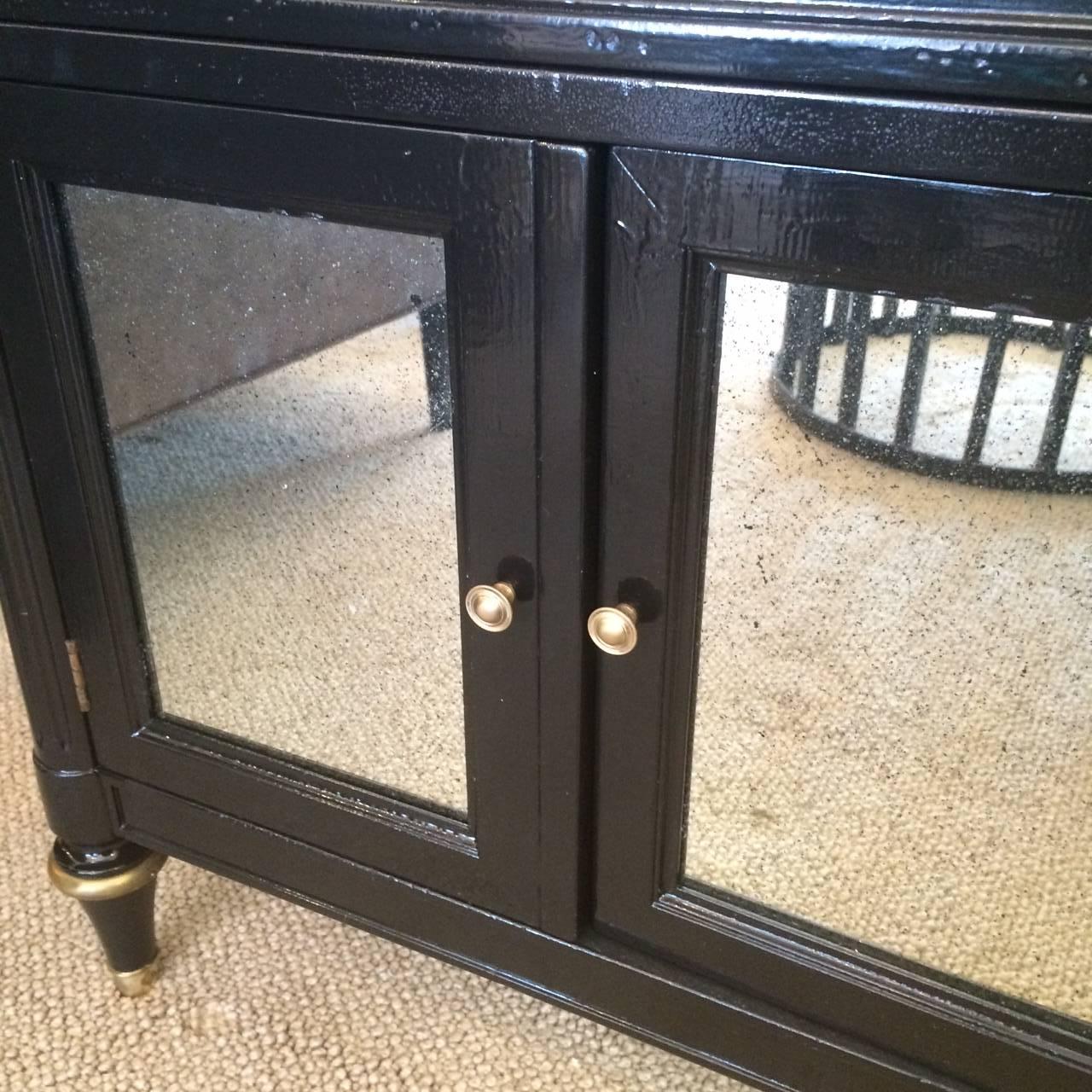 Two Midcentury neoclassical style nightstands or side table/cabinets by Kindel having a single drawer and two doors with storage inside. Panel doors have aged mirror fronts. Brass embellishments. A small hole has been drilled in the backs to allow