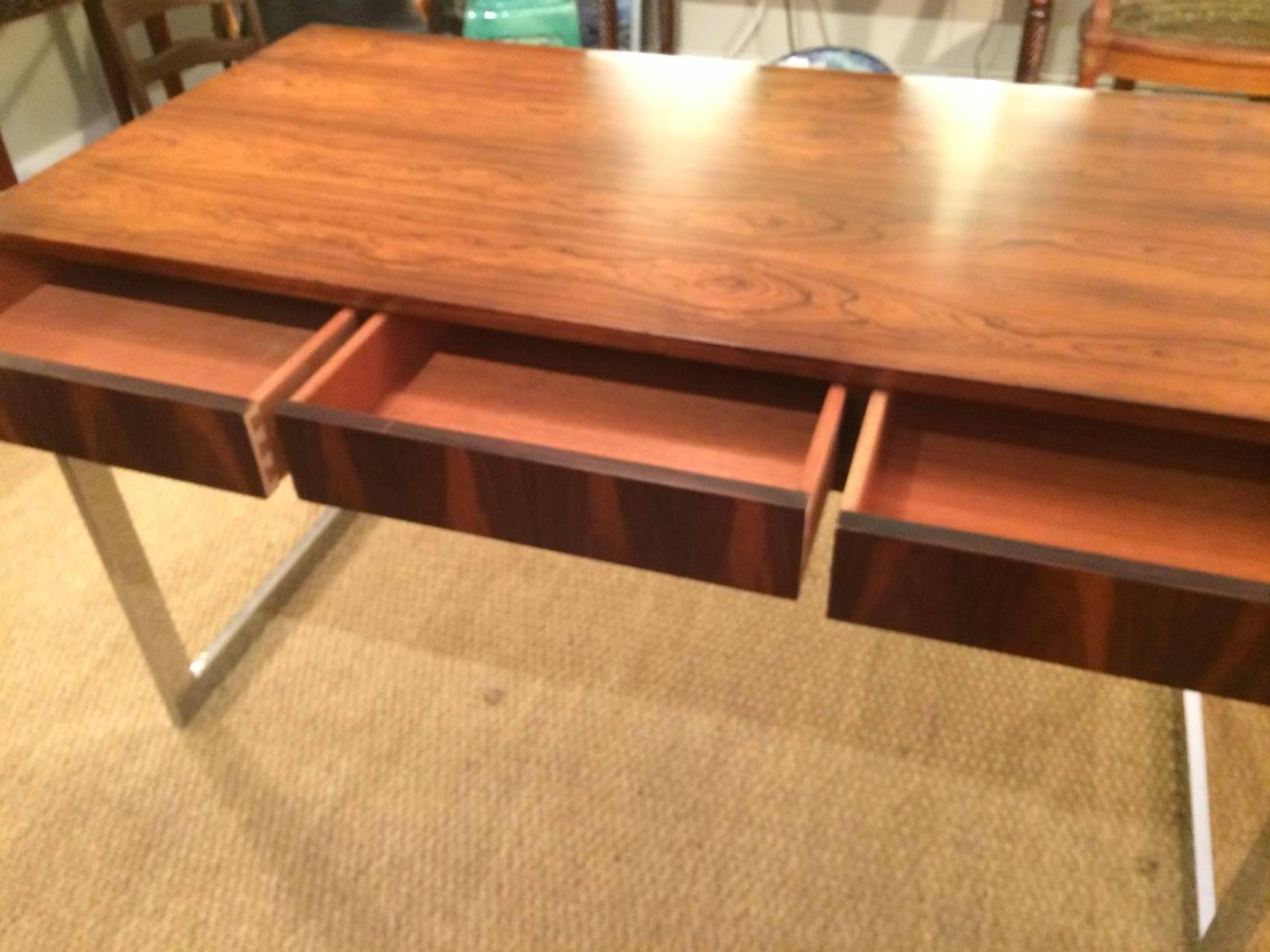 Rosewood veneer desk in the style of Milo Baughman, 1960s, with three working drawers resting on a chrome base connected by a cross-stretcher. Nice low lustre finish. Finished on the back so it can float in a room. 
