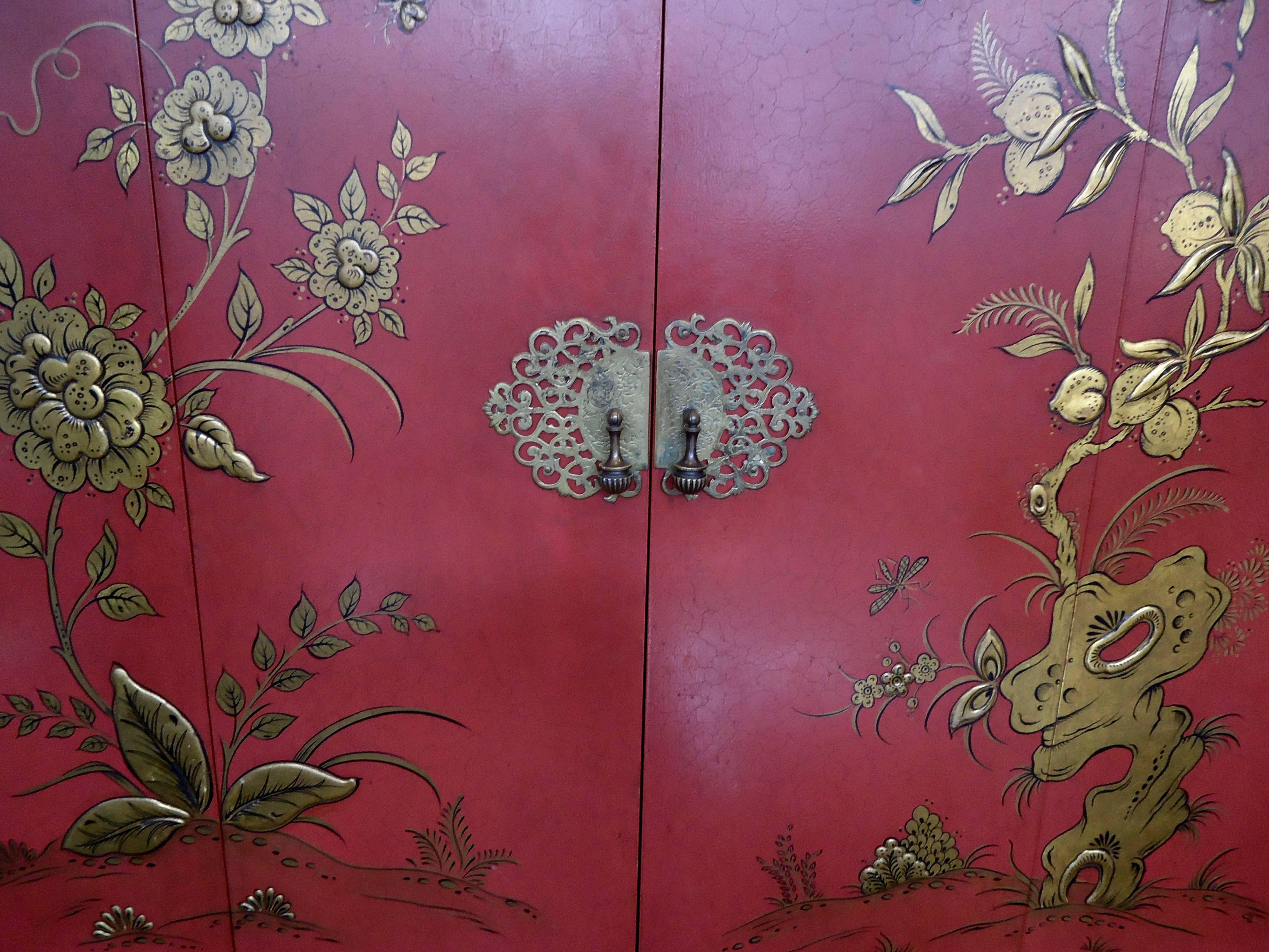 Chic Mid-Century chinoiserie and japanned bar in beautiful shade of coral. Mirrored interior and glass shelves recently added. Japanned exterior bifold doors. Gold leaf fretwork on corners and latice pattern on legs. Left side has inset light.