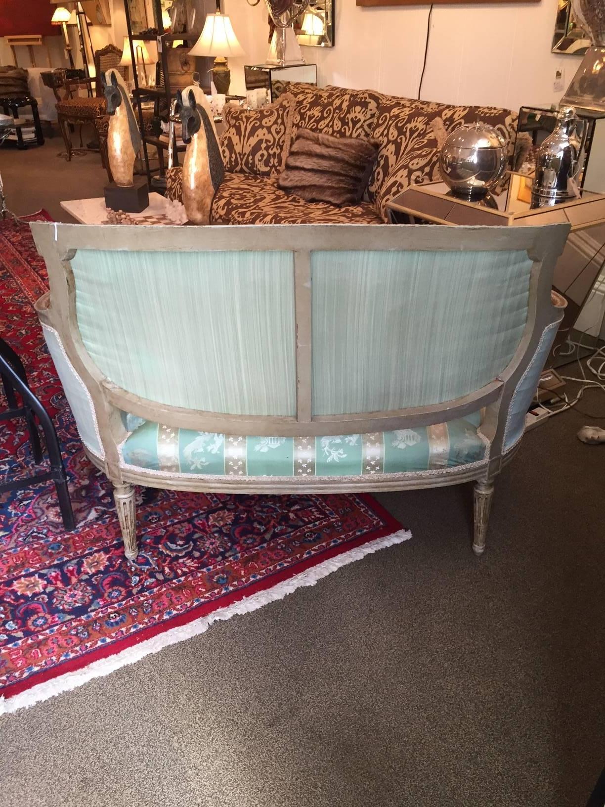 Very pretty French curved loveseat with carved mahogany painted white, fluted legs, and upholstered in a fancy celadon green and cream silk.

Seat: 23