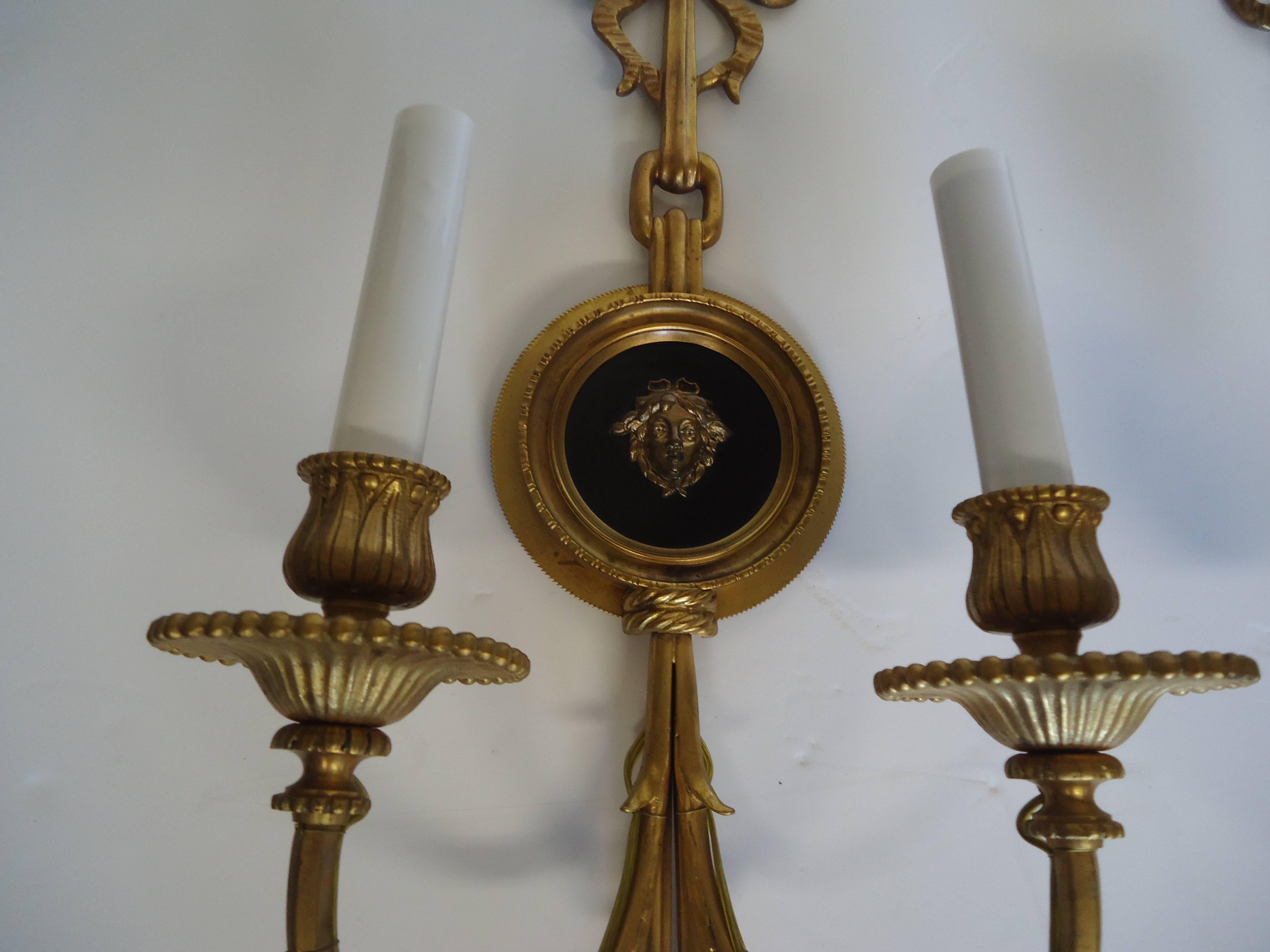 Lovely pair of bronze sconces with central Versace style medallions with nymph like faces against ebonized background, bows at the tops and tassels at the bottom, two arms with 60 watts each.