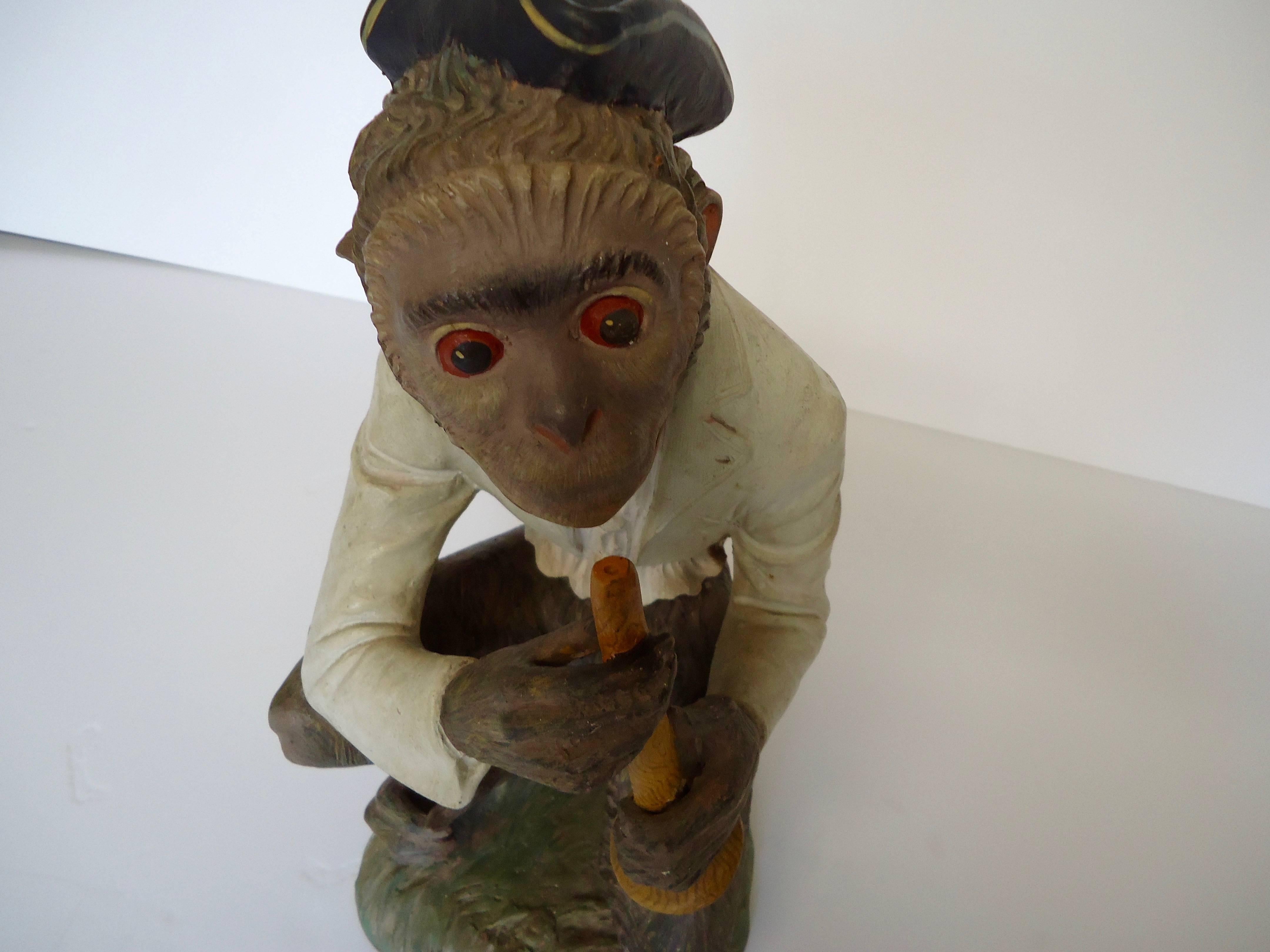 Rich in character, a wonderful hand-painted terracotta statue of a monkey with a pirate style hat sitting jauntily on his head, about to bring a horn to his lips. Marked 