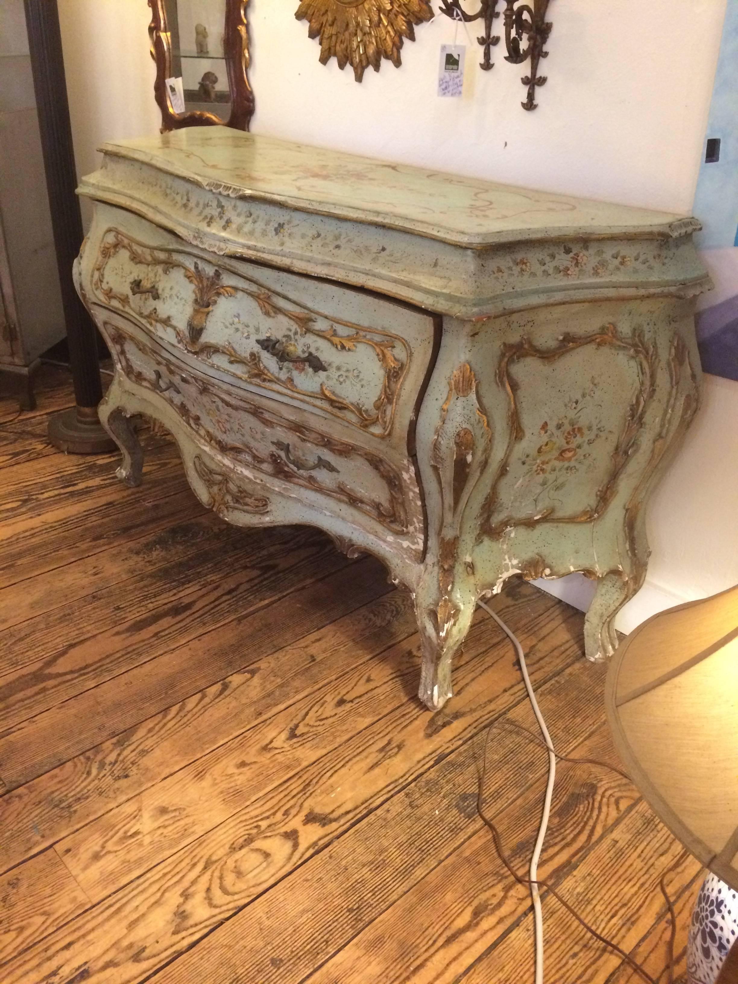Gorgeous and ornate Rococo bombay shaped commode, hand-painted in a soft celadon with gilt details and pastel flowers, with two large drawers. Original paint that is "chippy" in certain areas. Could be easily restored, but beautiful like