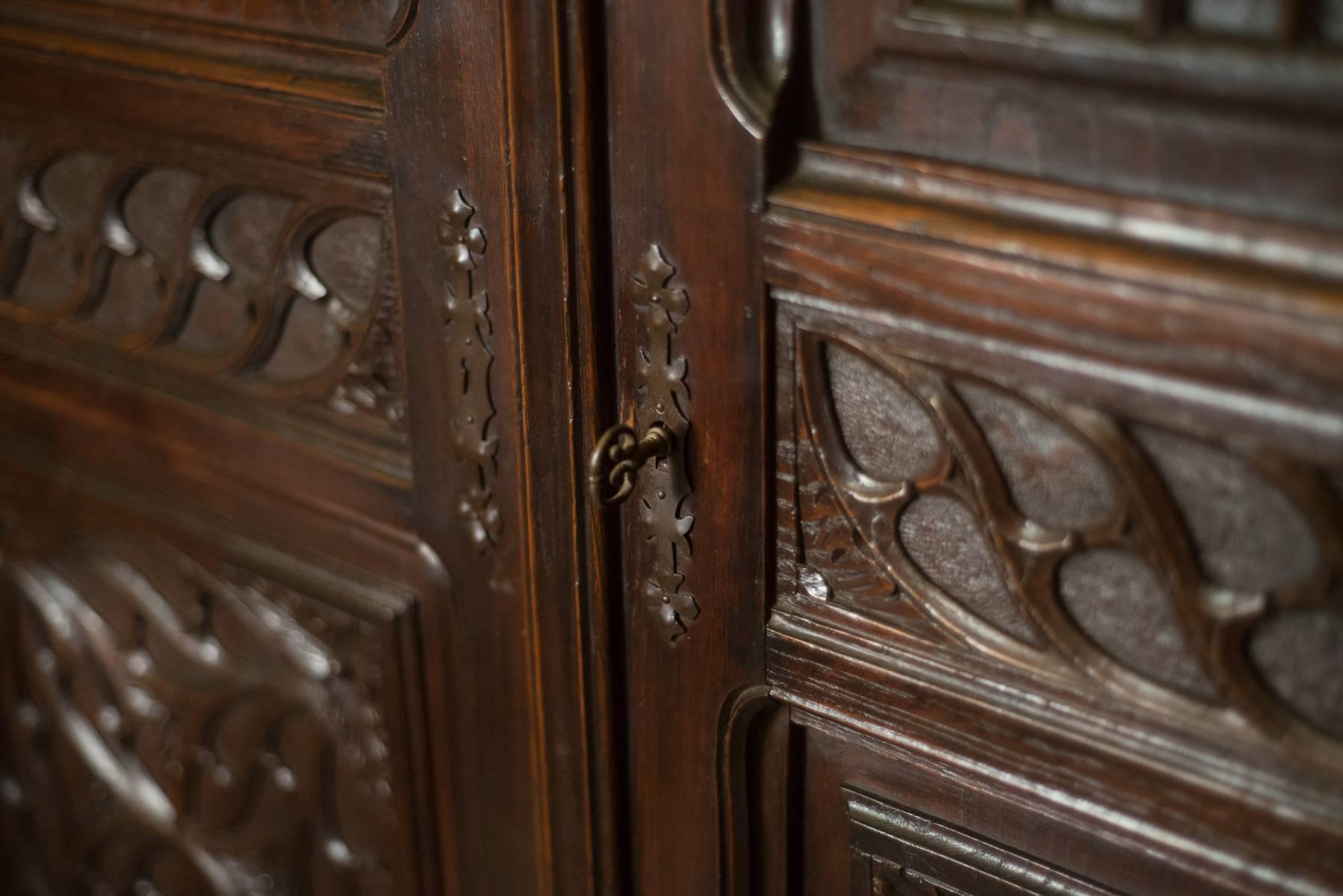 Magnificent chestnut cabinet with intricate Gothic motifs carvings and a gorgeous patina, round carvings on the doors imitate stained-glass windows and scroll work adorn the columns. Interior shelves for ample storage within.
 Breaks down for easy