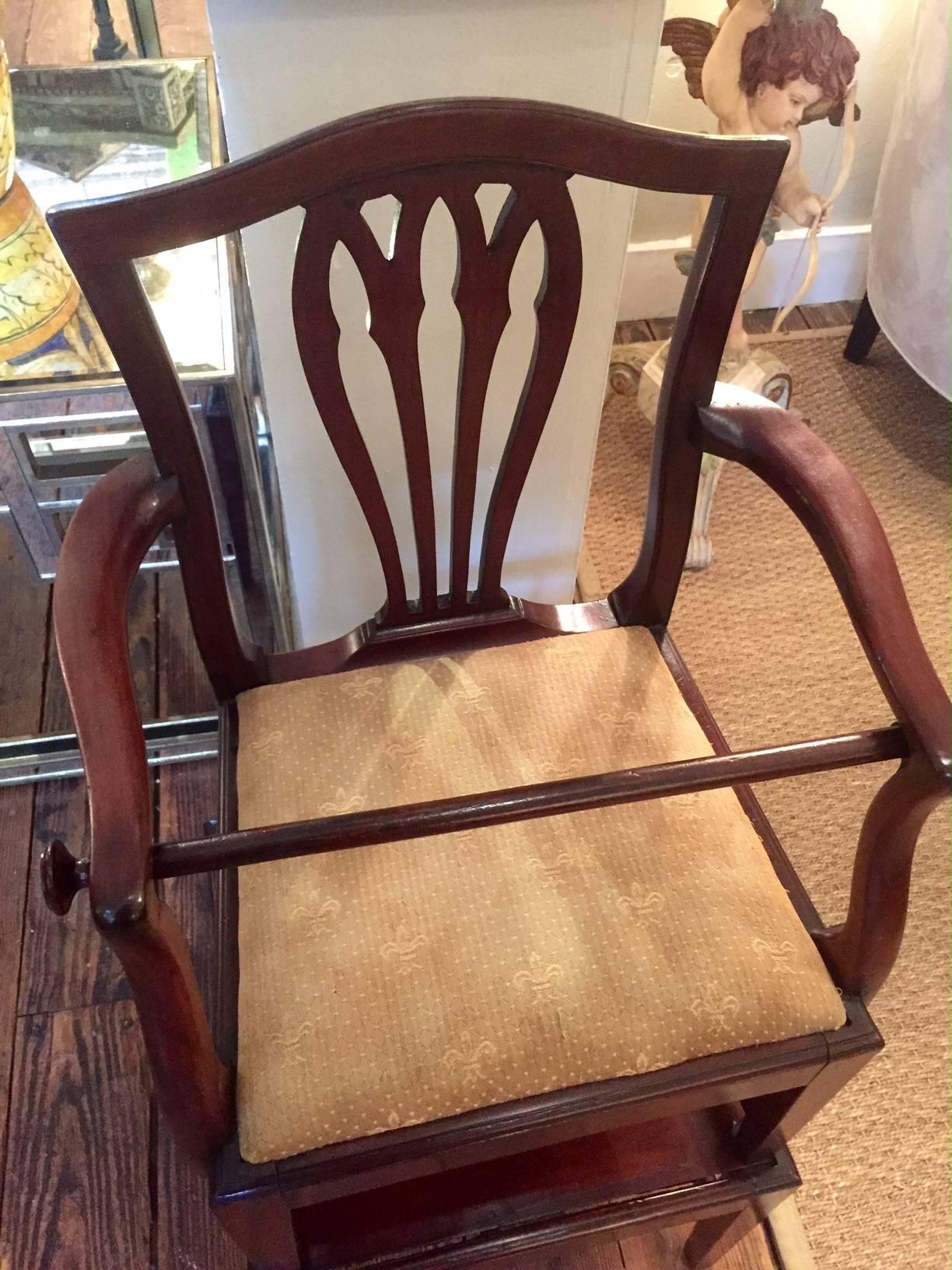Antique mahogany high chair in two parts, having a shield back arm chair with removeable retaining rod (cap on the right is doweled and pulls off) resting on square tapering legs connected by an H-stretcher, sitting on top of a similar platform held