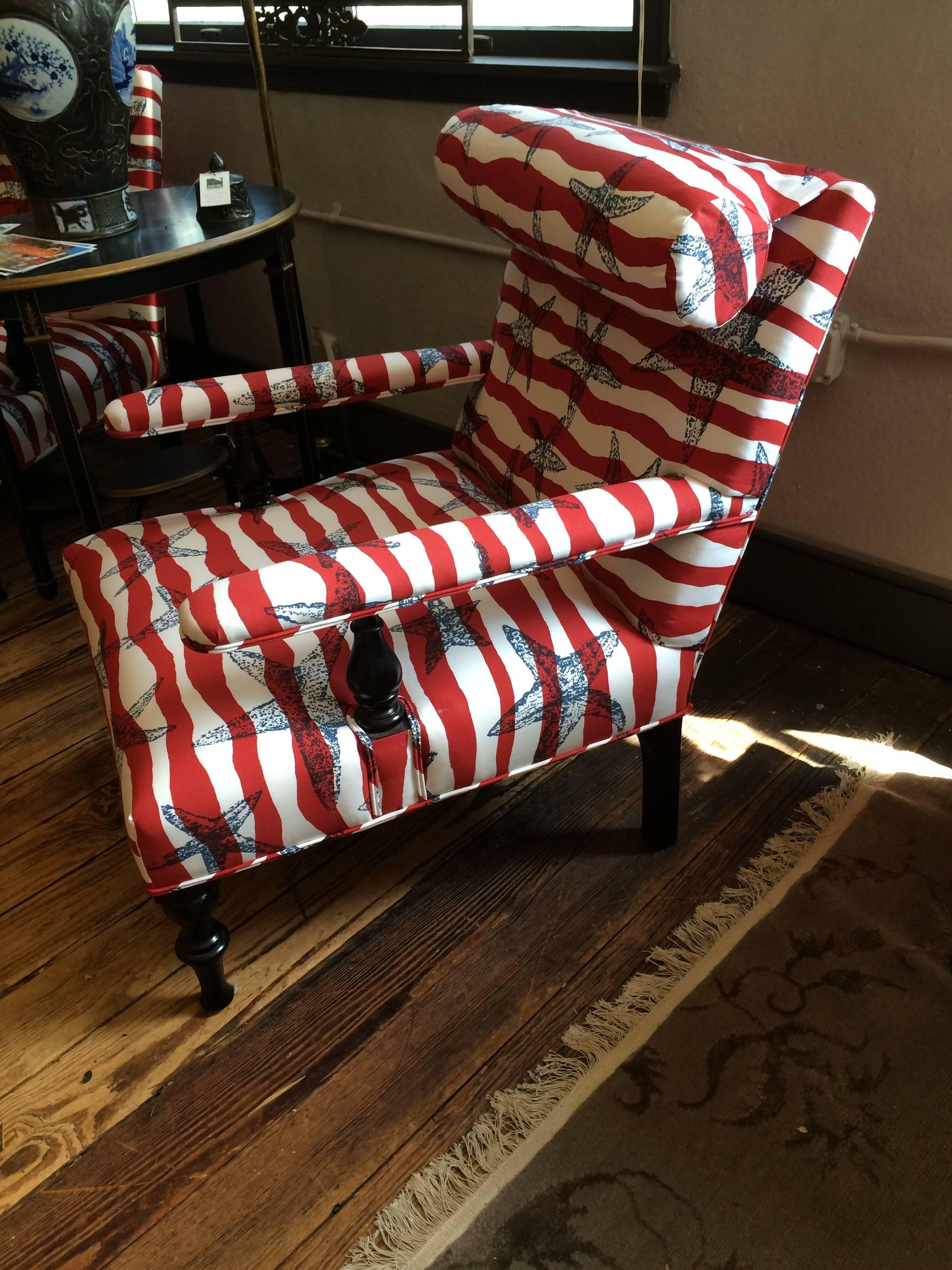 Sensational pair of large low slung club chairs having mahogany turned legs, imaginatively upholstered in patriotic hand screened Tillett fabric on the front and solid red on the back. Fun round pillows attached at the head rest for a flashy