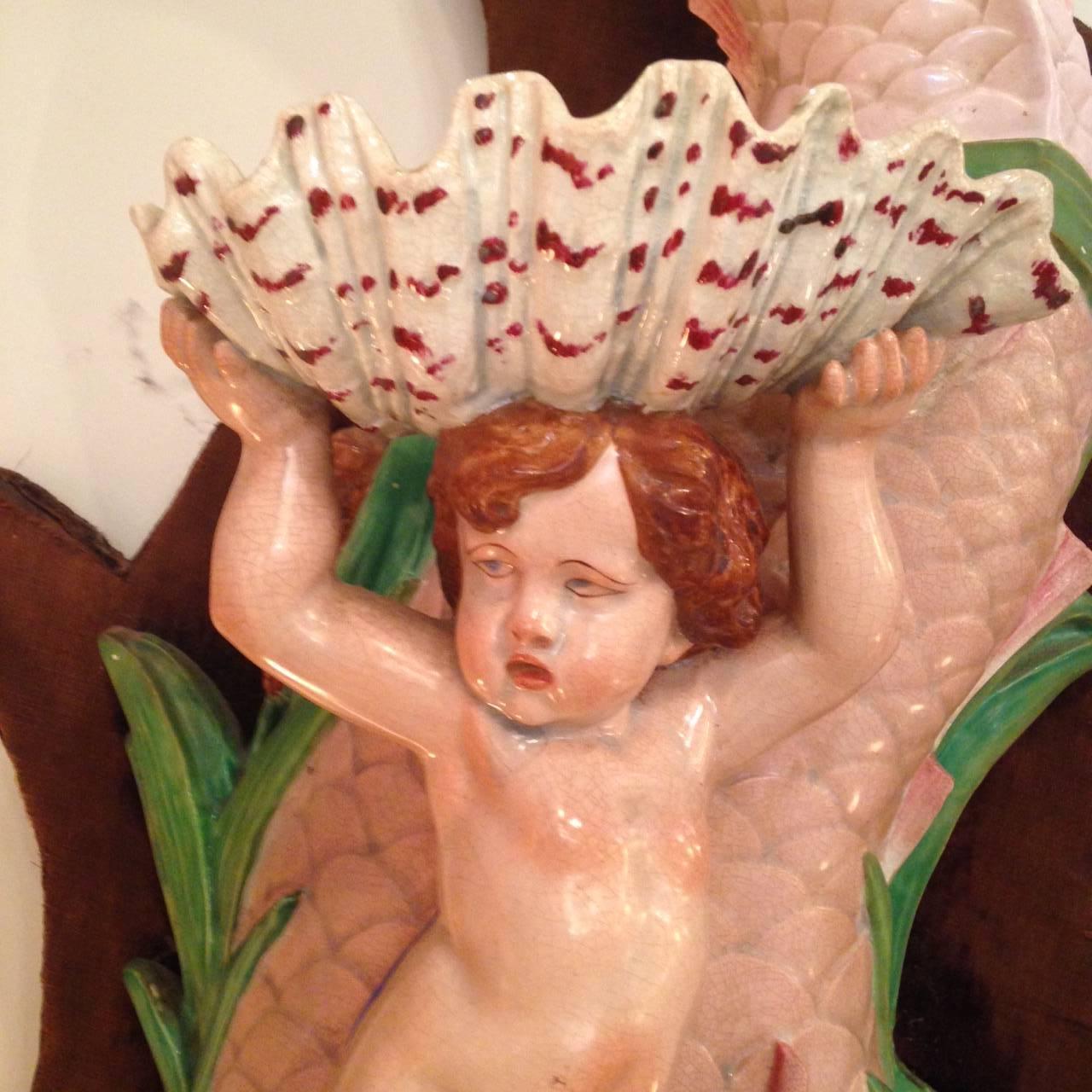 French Majolica Lavabo, mid-19th century in three parts, 
depicting a cherub holding a scallop shell as he rides a dolphin 
surrounded by grasses and cattails. Color palette is a magical pastel ambrosia of pinks, light green and gold. Appears to