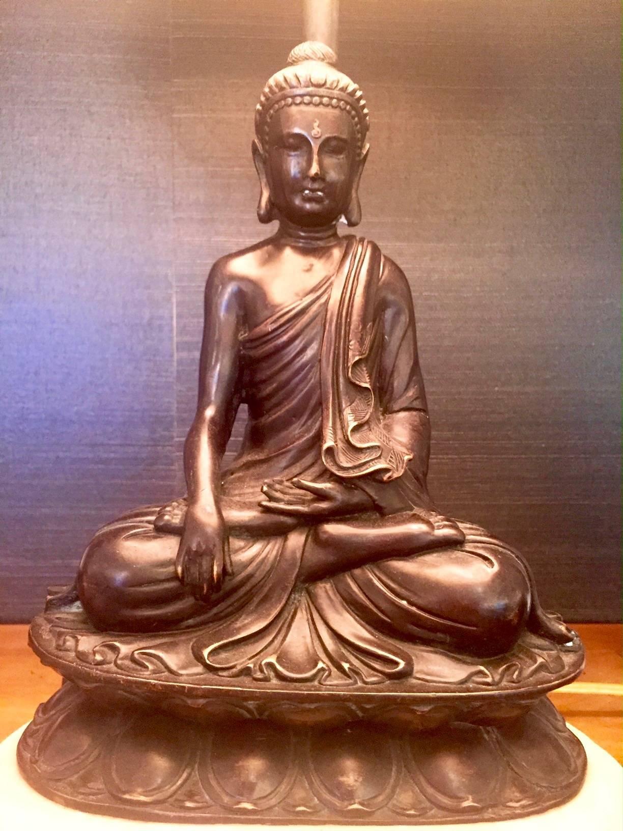 A gorgeous objet d'art consisting of a bronze patina metal Buddha resting on a cream colored stone base, topped with a custom shade with gold and cream striped lining.
10.5