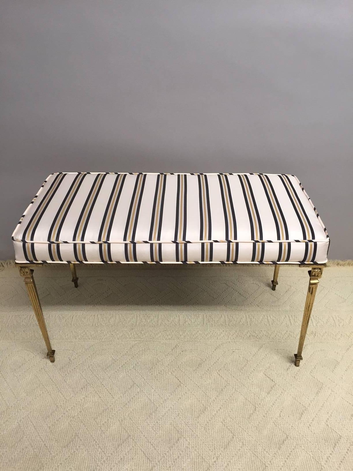 Base is glamorous brass with reeded legs and lion cartouches, newly upholstered in snappy black, gold and cream striped silk.