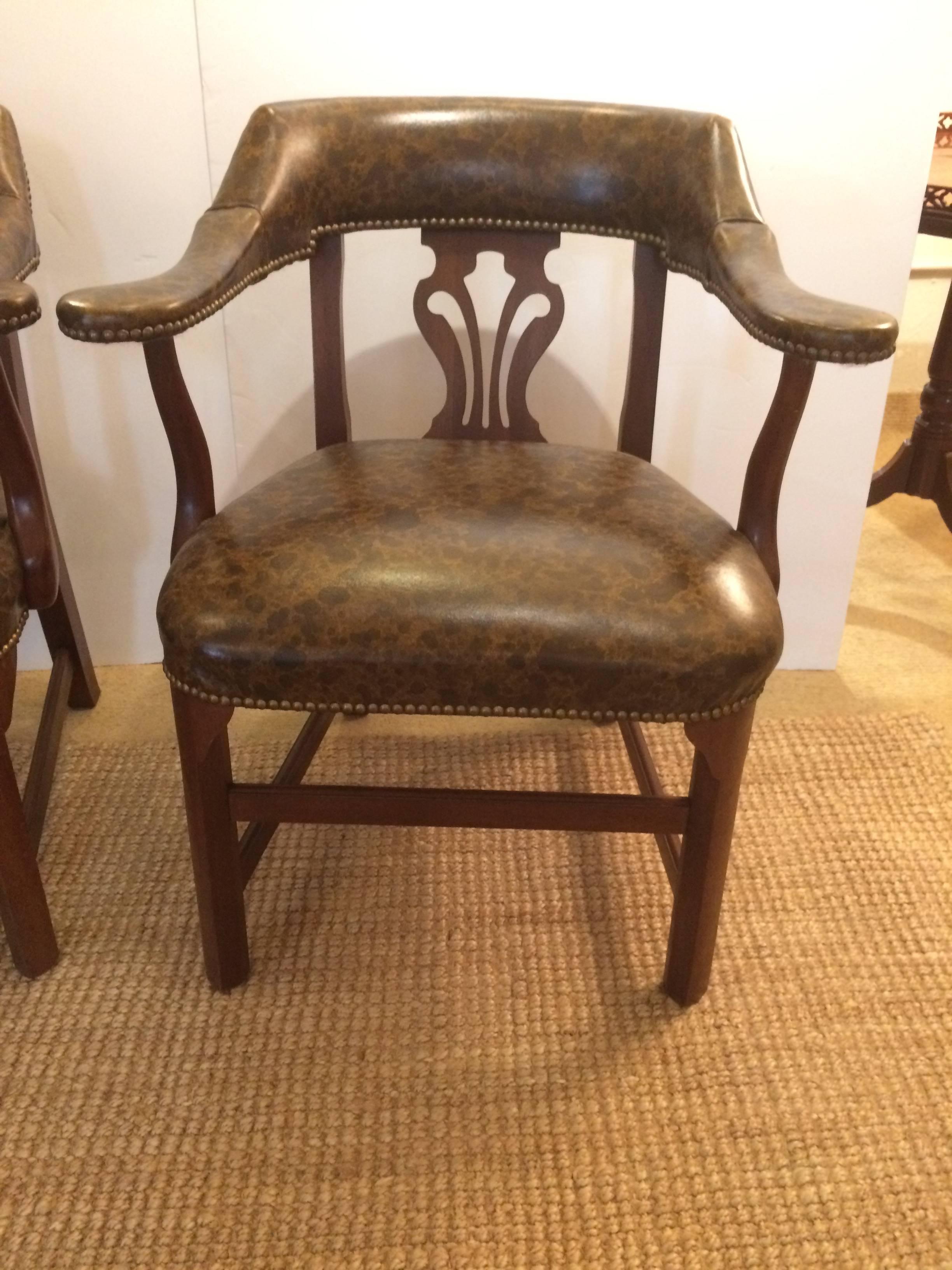 Two masculine club chairs having mahogany curved back and arms with decorative fleur di lis style cut out, upholstered in a rich two tone brown leather that looks like tortoiseshell, all finished in brass nailheads.