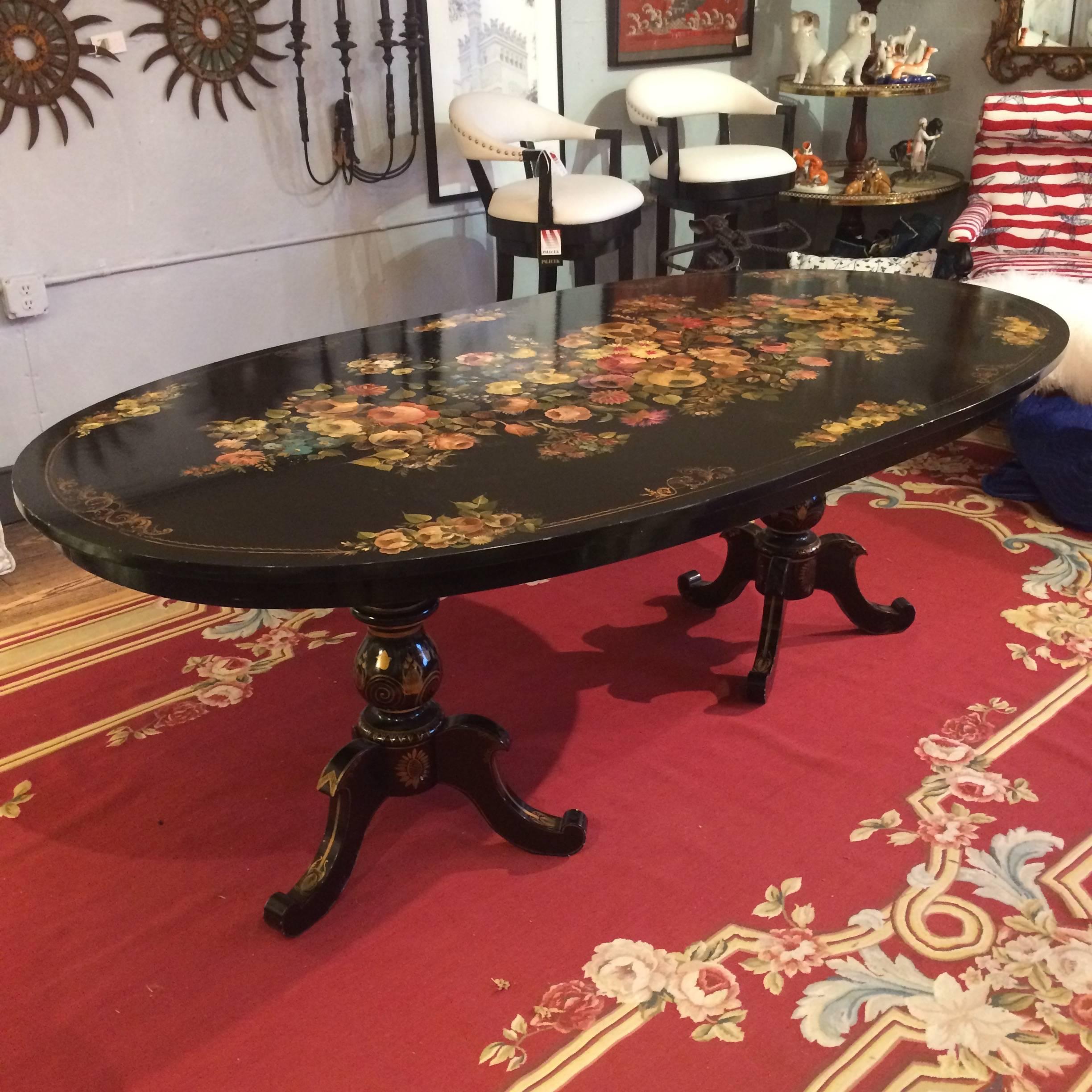 One of a kind charming oval dining table having black background and meticulous hand-painted floral decoration in pinks, green, cream and gold, with two tripod pedestals. Fully restored Victorian dining chairs complete the set, having same color