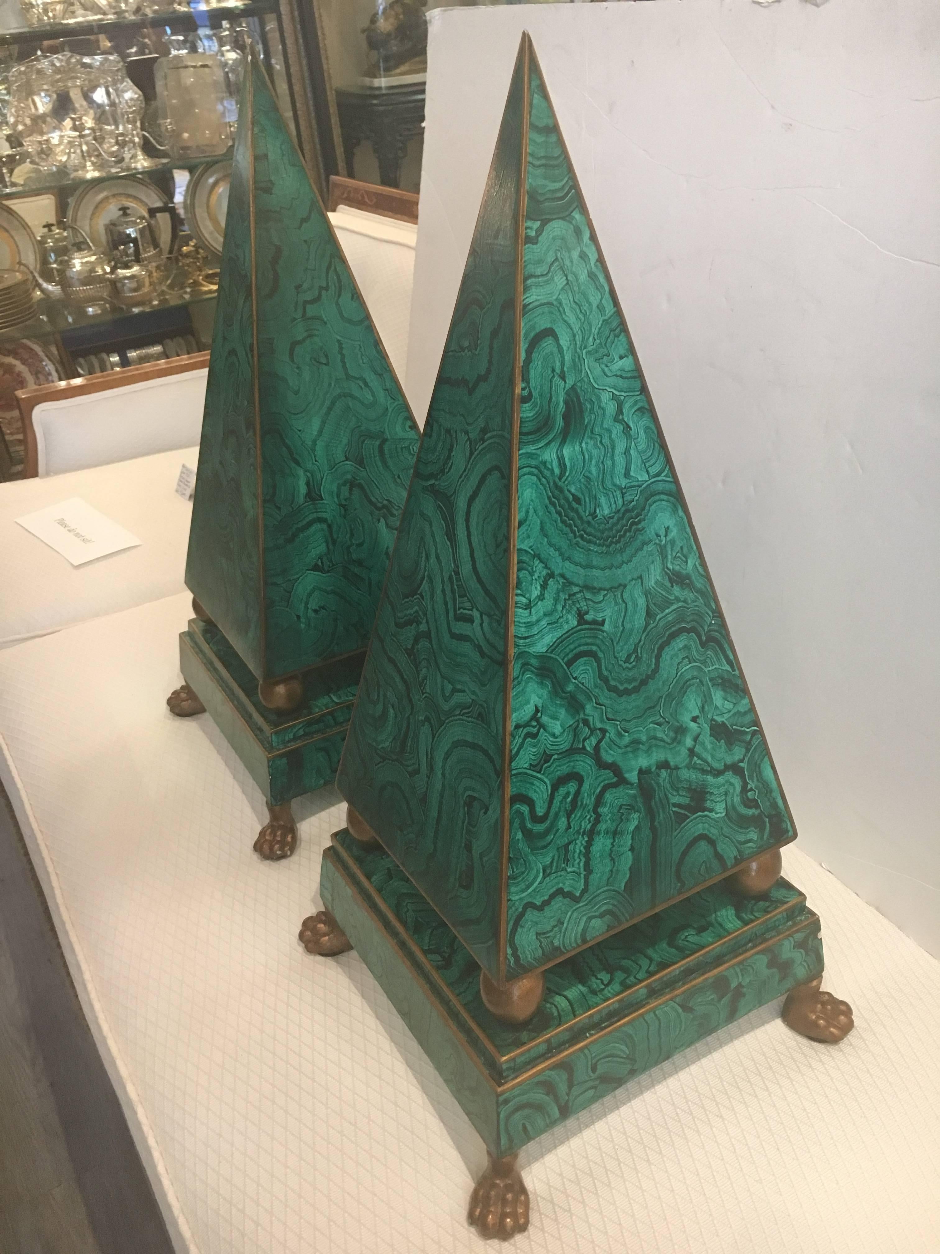 Ultra chic faux malachite obelisks in the style of Tony Duquette. Hand-painted in a rich, emerald green malachite with gilt edges, obelisks are made of wood with brass lion paw feet.
