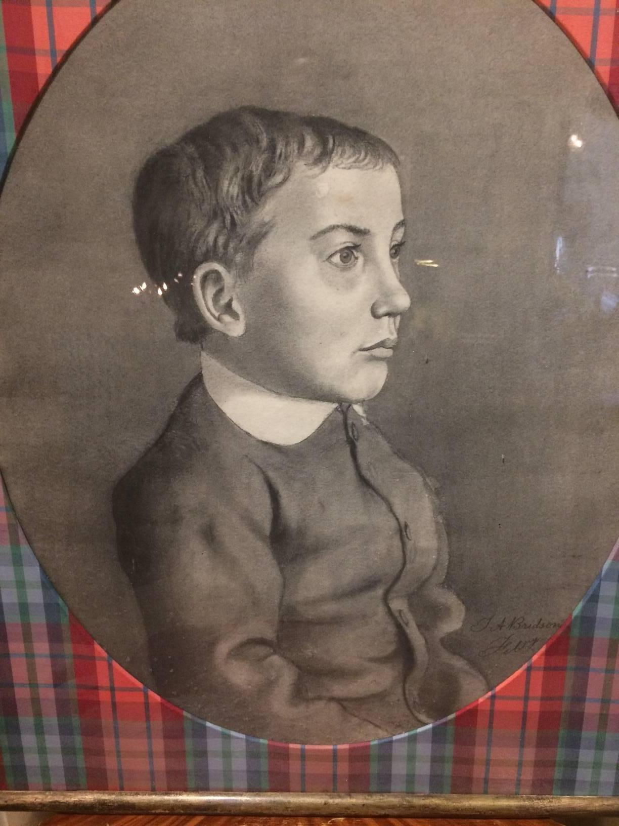 19th century charcoal portrait of a pensive little boy imaginatively matted as an oval surrounded by fancy plaid taffeta and a vintage giltwood frame with original wavy glass. Signed lower right L A Bridson.