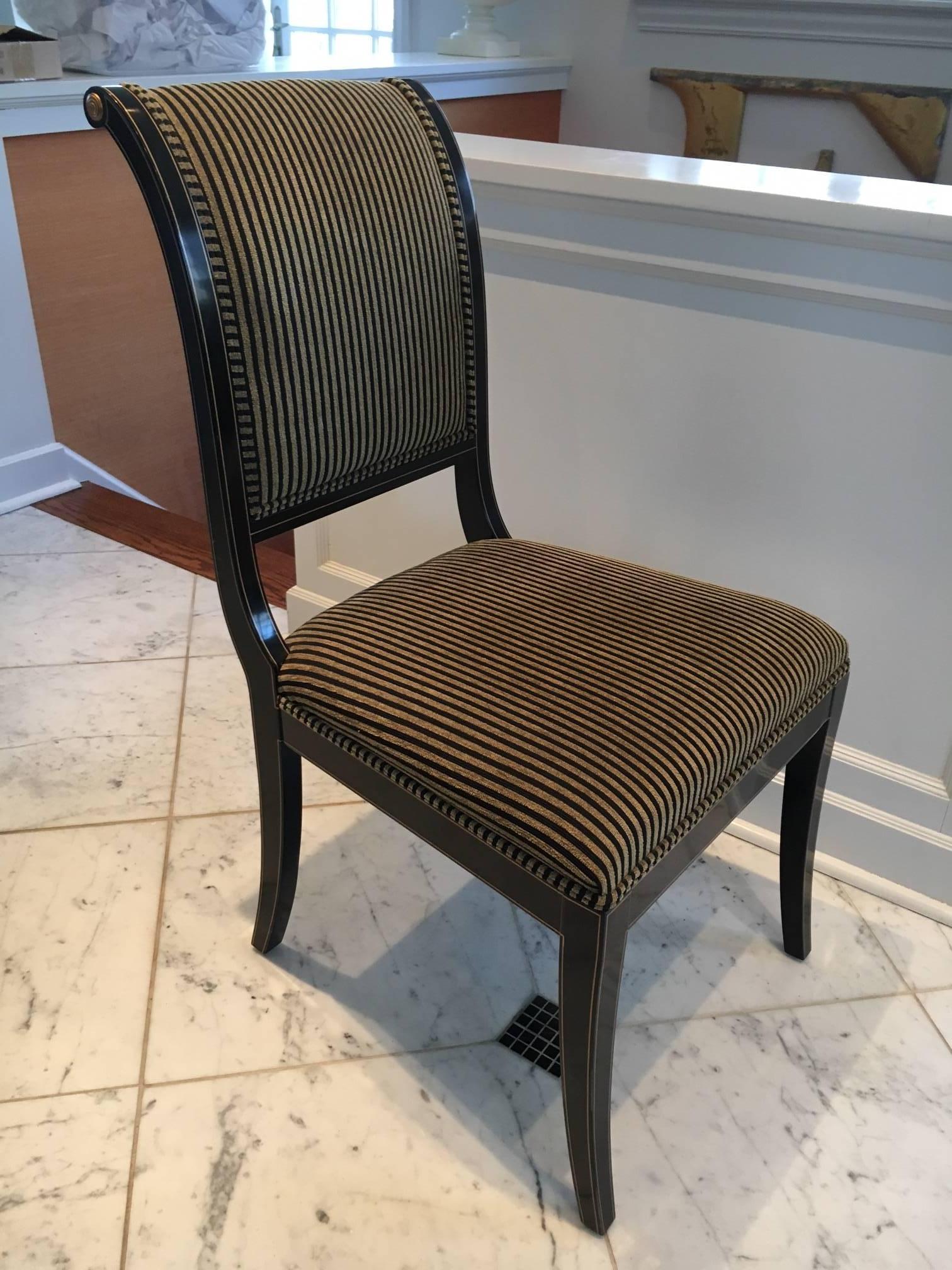 Chic set of six Regency style dining chairs by Kindel. Lacquer black finish outlined in gilt detail terminating with gilt medallion on top and arms (see photo). Upholstered in a black and camel stripe in a silk or cotton blend. Double welt. Four