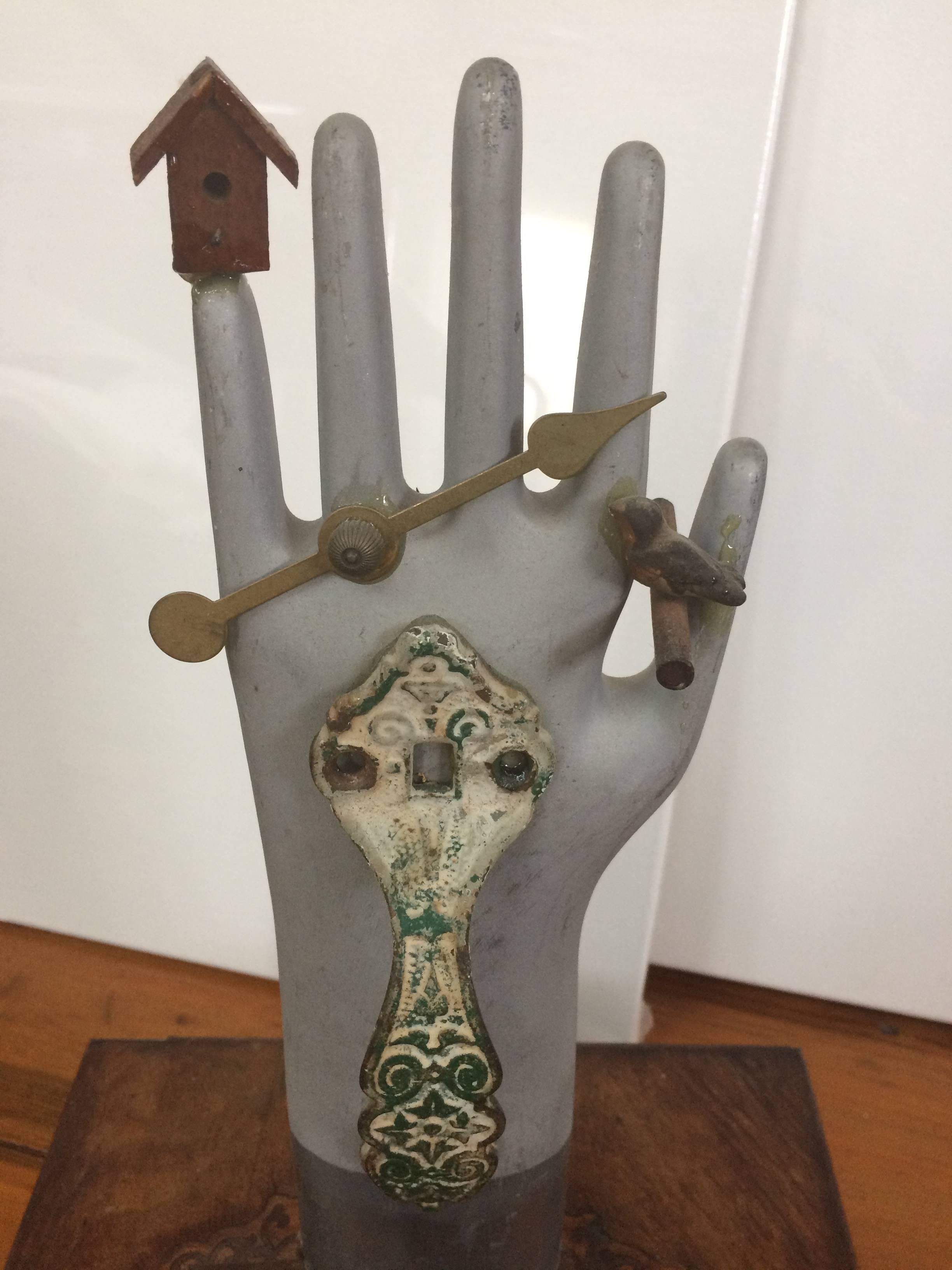 Une œuvre d'art qui part d'une boîte ancienne en bois incrusté et qui devient un assemblage comprenant un moule de gant en métal vintage qui sert de moyen d'ouverture de la boîte, des morceaux d'un coucou déconstruit, une poignée en vert-de-gris