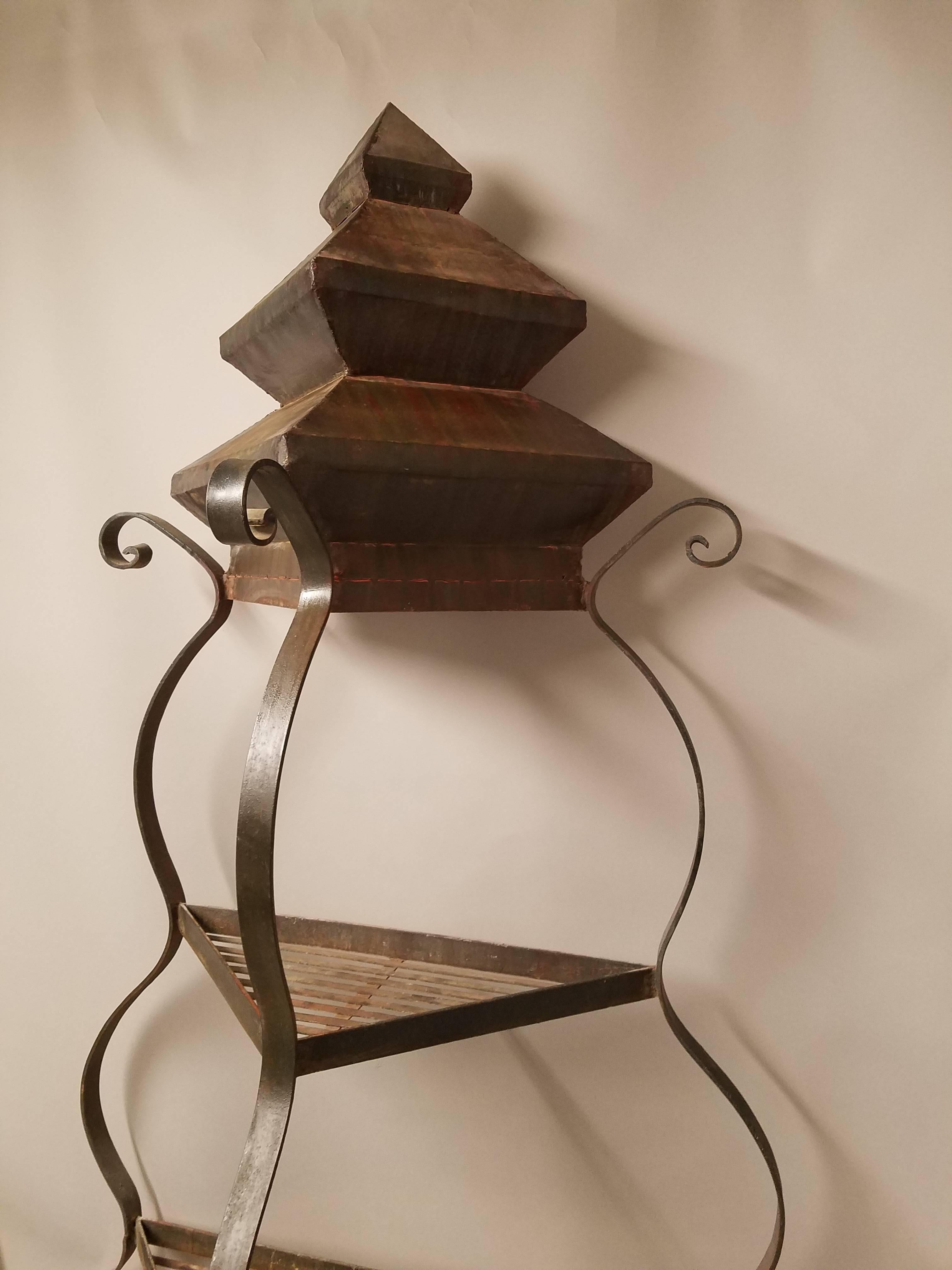 Three triangular shelves on a scrolling frame. Natural oxidation. Can be used indoors or outside for plants or display of objects. Top is a chic pagoda of steel.