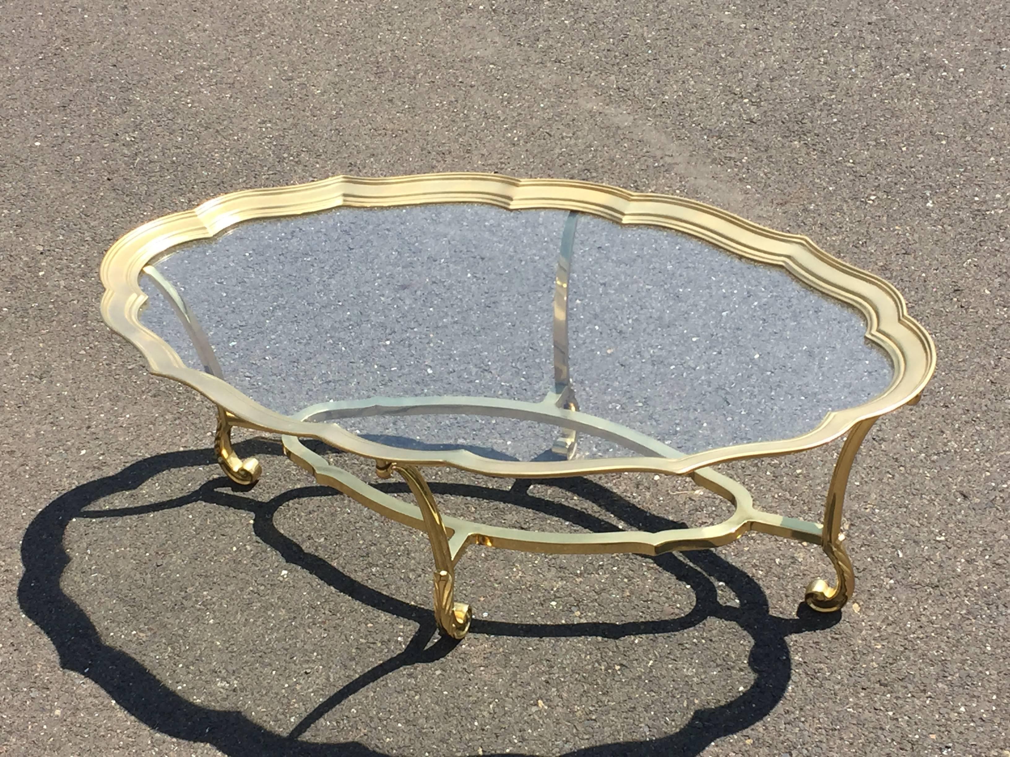 Elegant brass coffee table with lovely scalloped top and curlicued feet, having a clear glass top.