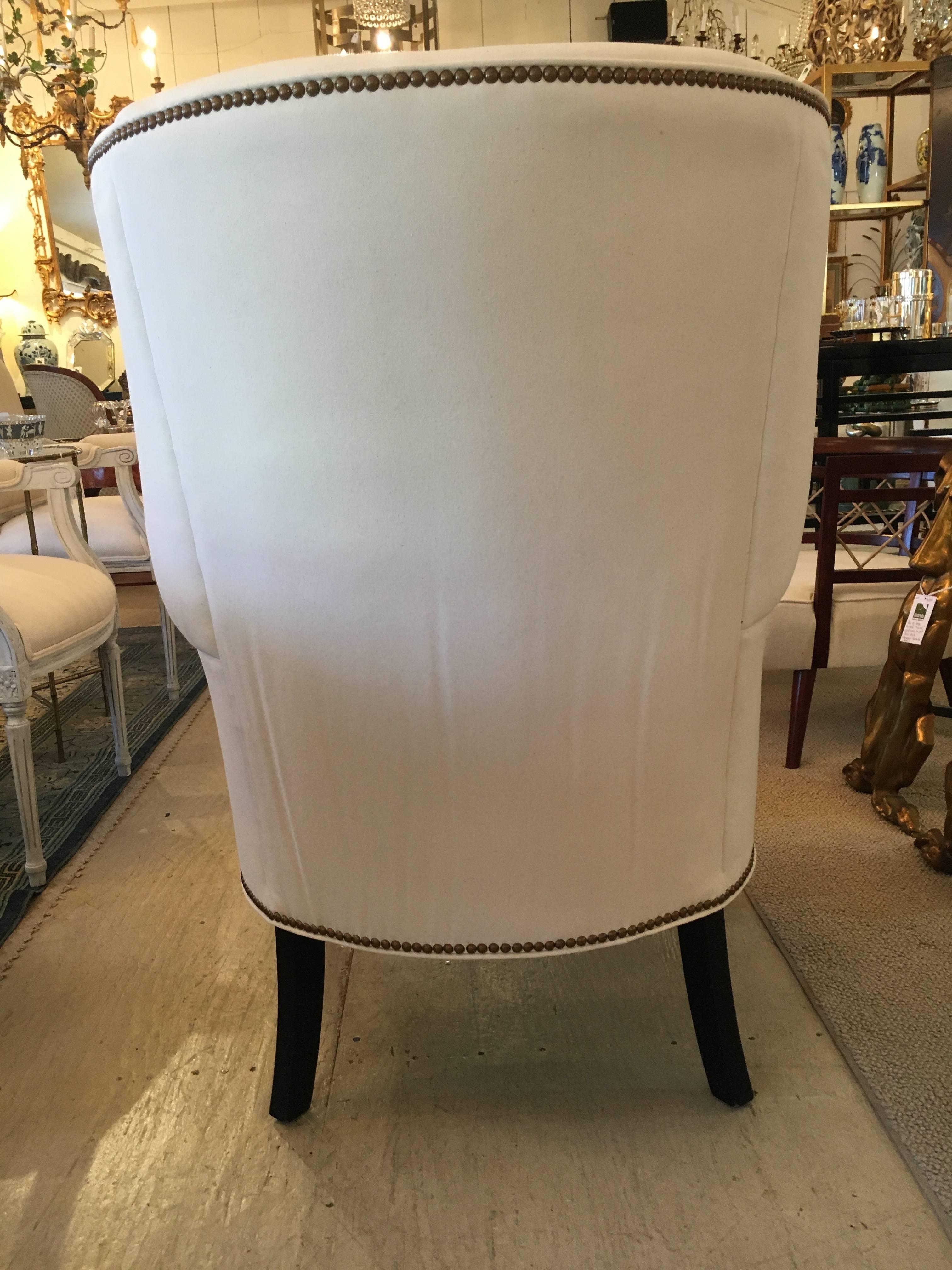 Sophisticated pair of wing chairs with ebonized legs, newly upholstered in white cotton duck and French brass nailheads.  Seat depth 21.5". Arm height is 26". 
